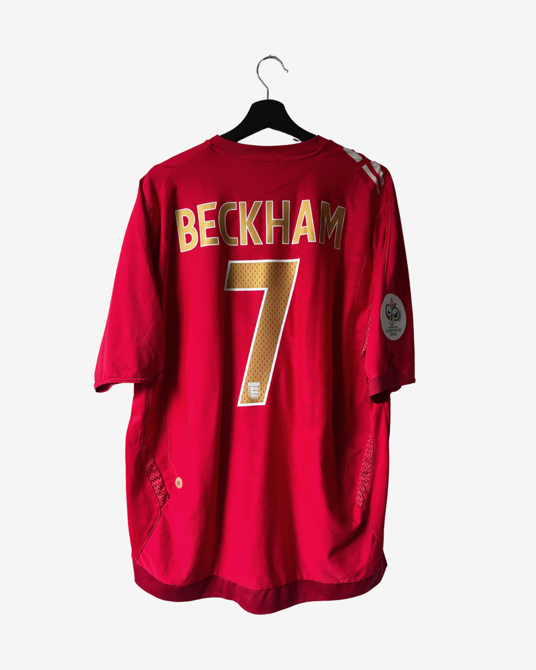 A red short-sleeve Beckham jersey with the name 'BECKHAM' and number '7' in gold on the back, hanging on a black hanger against a light gray background.