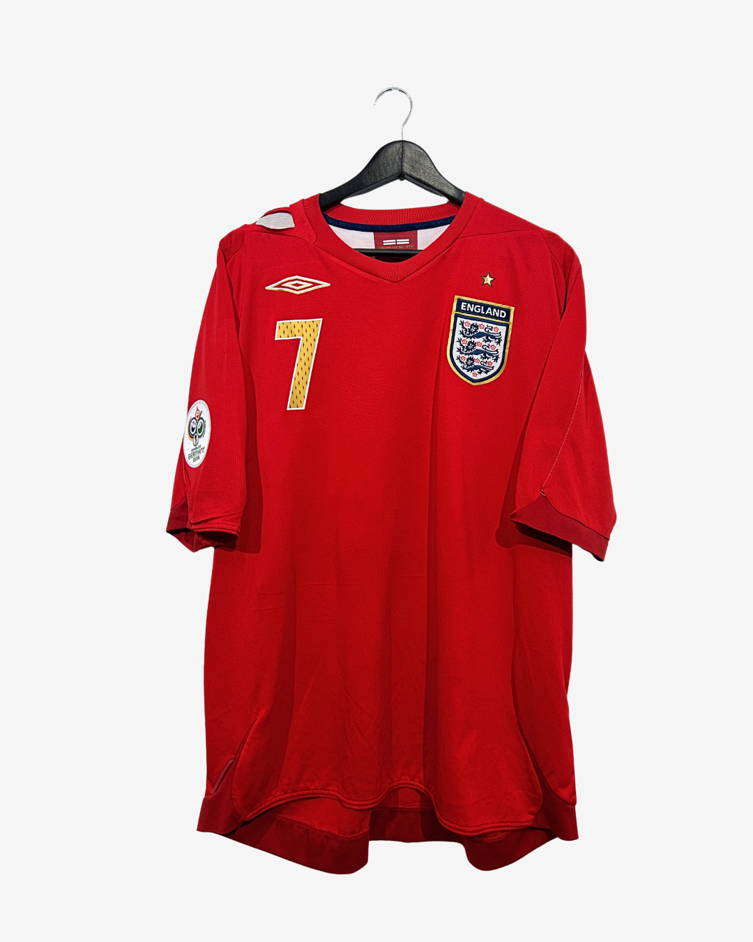 A red England national football team jersey with the number 7 on the front, hanging on a black hanger against a light gray background.