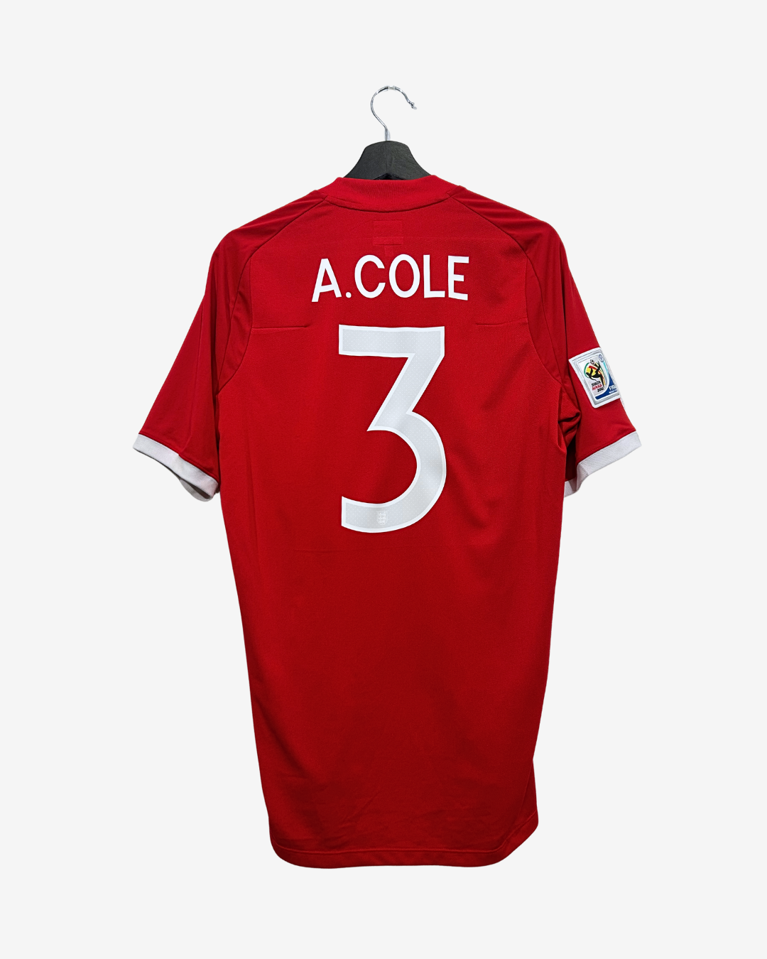 A red short-sleeve soccer jersey hanging on a black hanger against a light gray background. The back of the shirt features the name 'A.