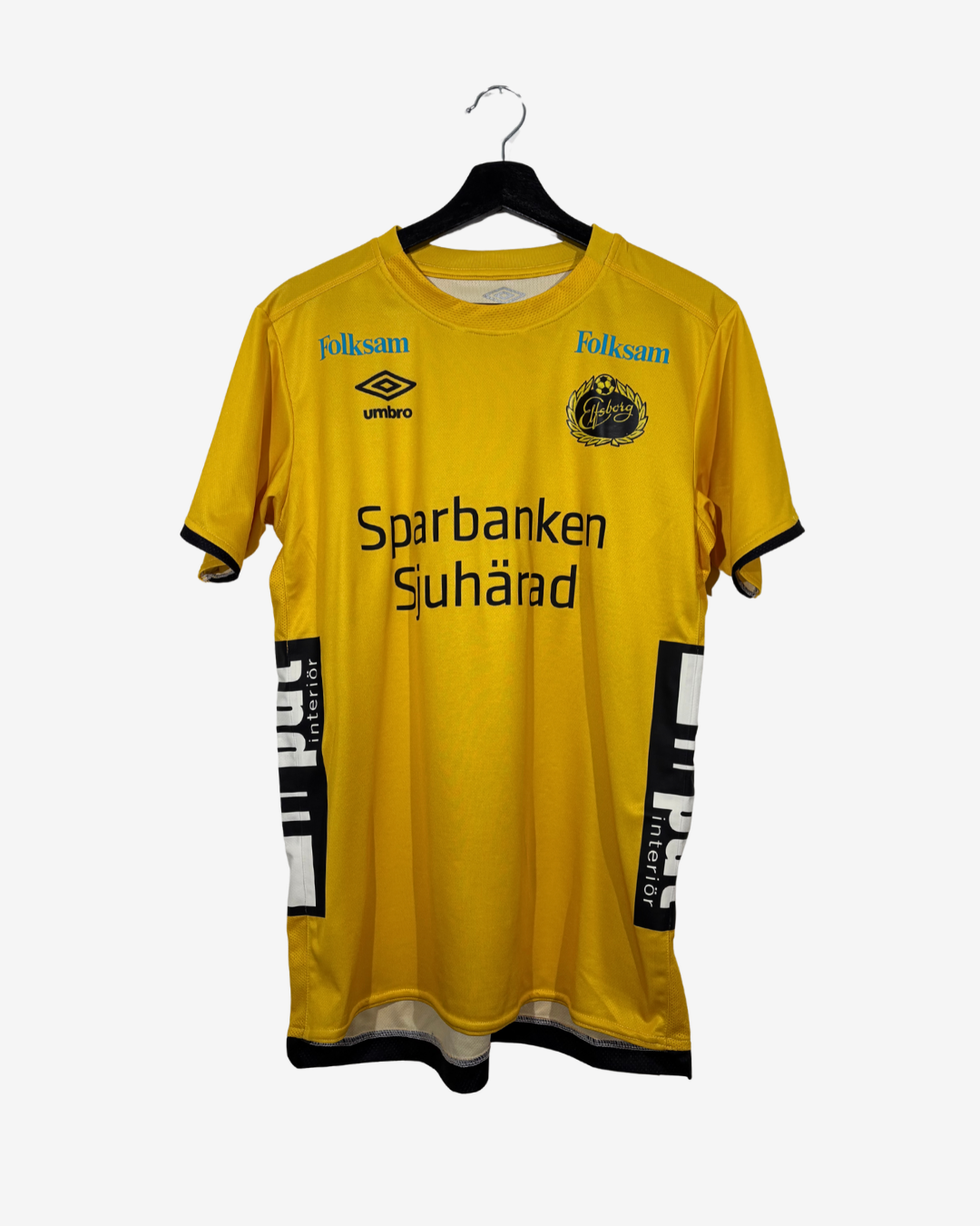 A yellow short-sleeve football jersey hanging on a black hanger against a light gray background. The jersey features 'Sparbanken Sjuhärad' printed across the chest, with 'folksam' logos on the shoulders and the 'umbro' logo below it.