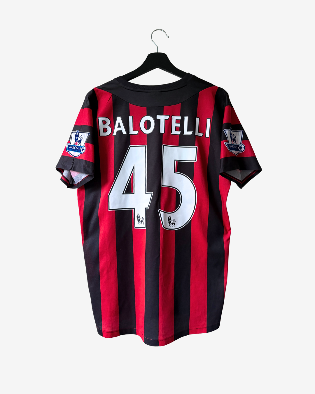 Manchester City Balotelli number 45 back view soccer jersey hanging on a black hanger against a light gray background.
