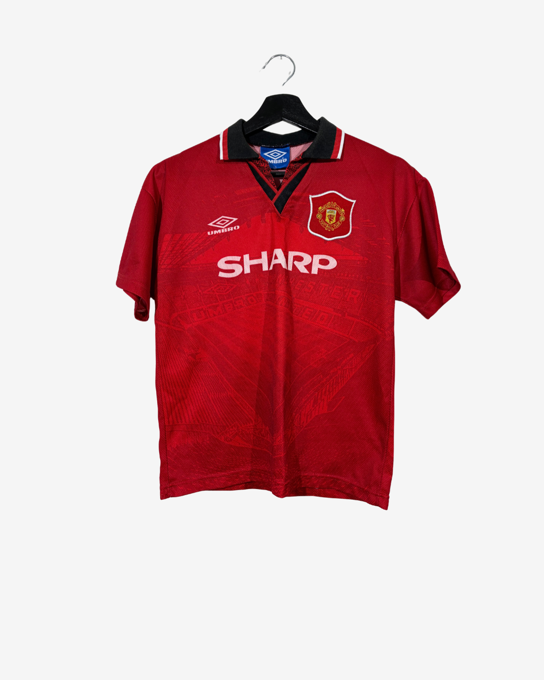 A vintage red Manchester United short-sleeve soccer jersey by Umbro, featuring the 'SHARP' sponsor logo across the chest, hanging on a black hanger against a light gray background.