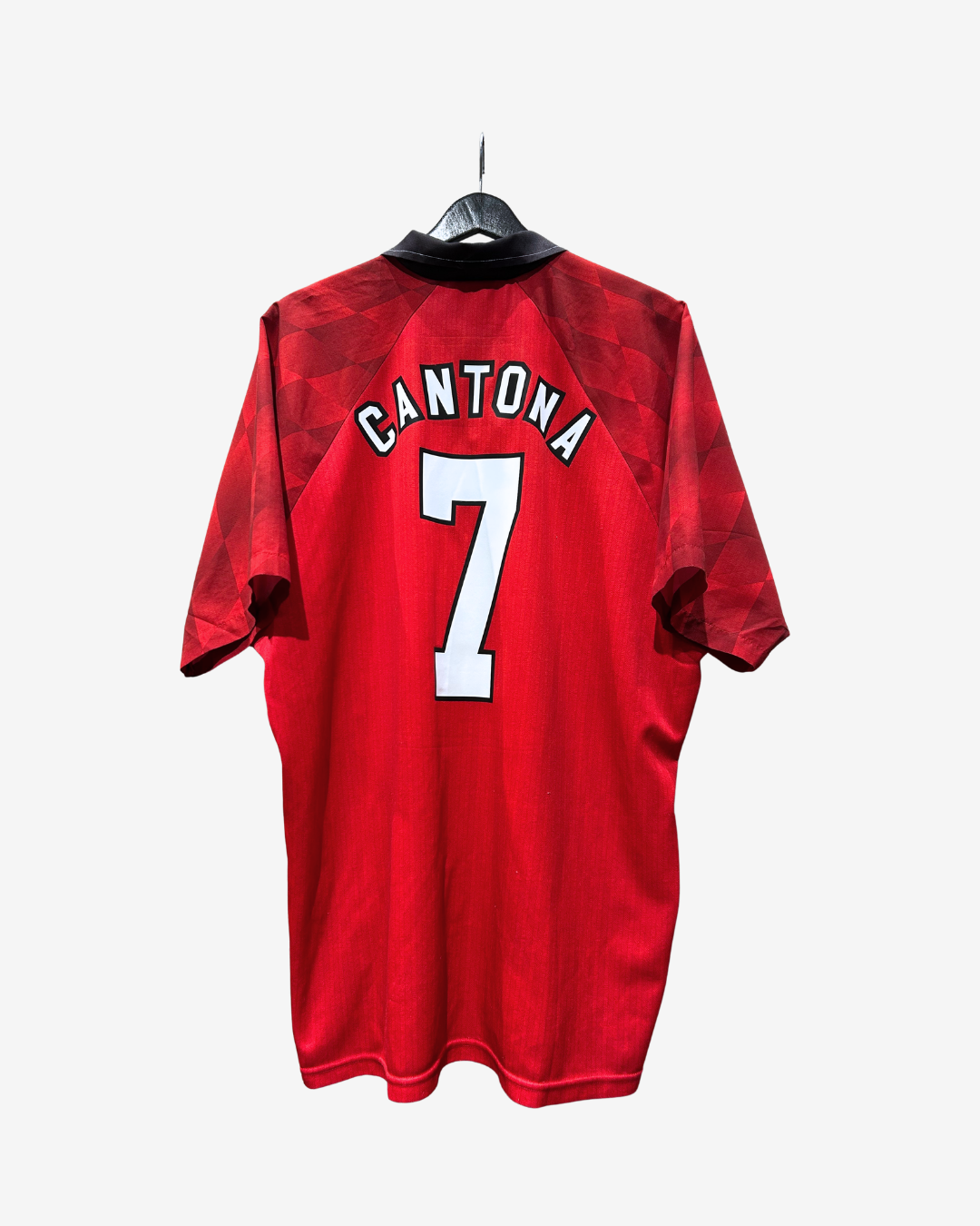 A red short-sleeve soccer jersey hanging on a black hanger against a light gray background. The back of the jersey features the name 'CANTONA' in white arched letters above a large white number '7' with a black outline.