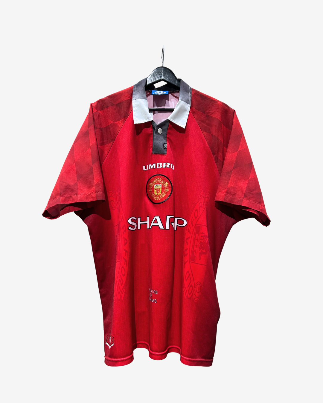 A red Manchester United short-sleeve polo shirt with a white collar, hanging on a black hanger against a light gray background. The shirt features the Manchester United crest on the chest, the 'UNIBRAND' sponsor logo, and 'SHARP' in white text.