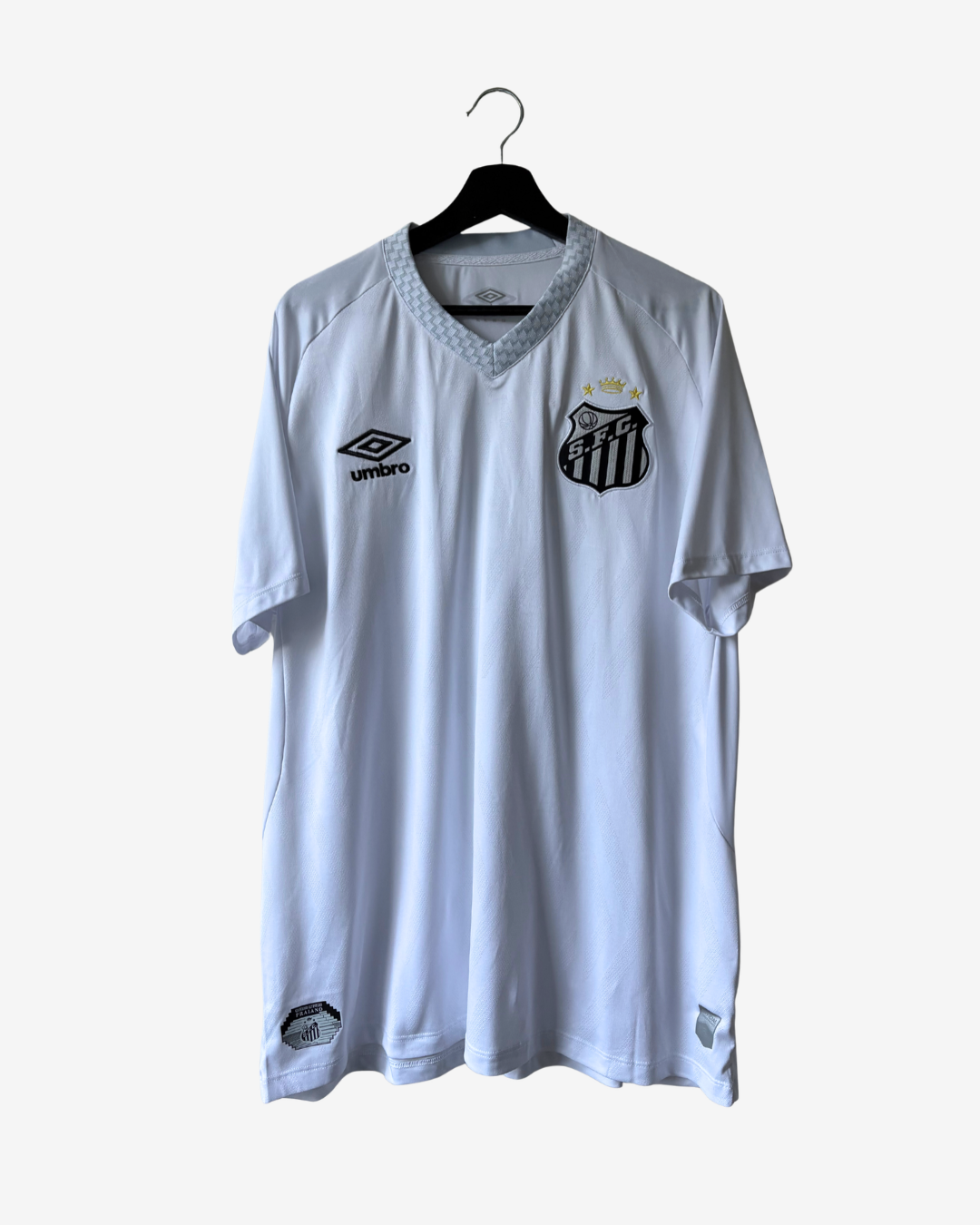 A white vintage Umbro Santos FC soccer jersey hanging on a black hanger against a light gray background. The jersey features the black Umbro logo on the right chest and the Santos FC crest on the left chest.