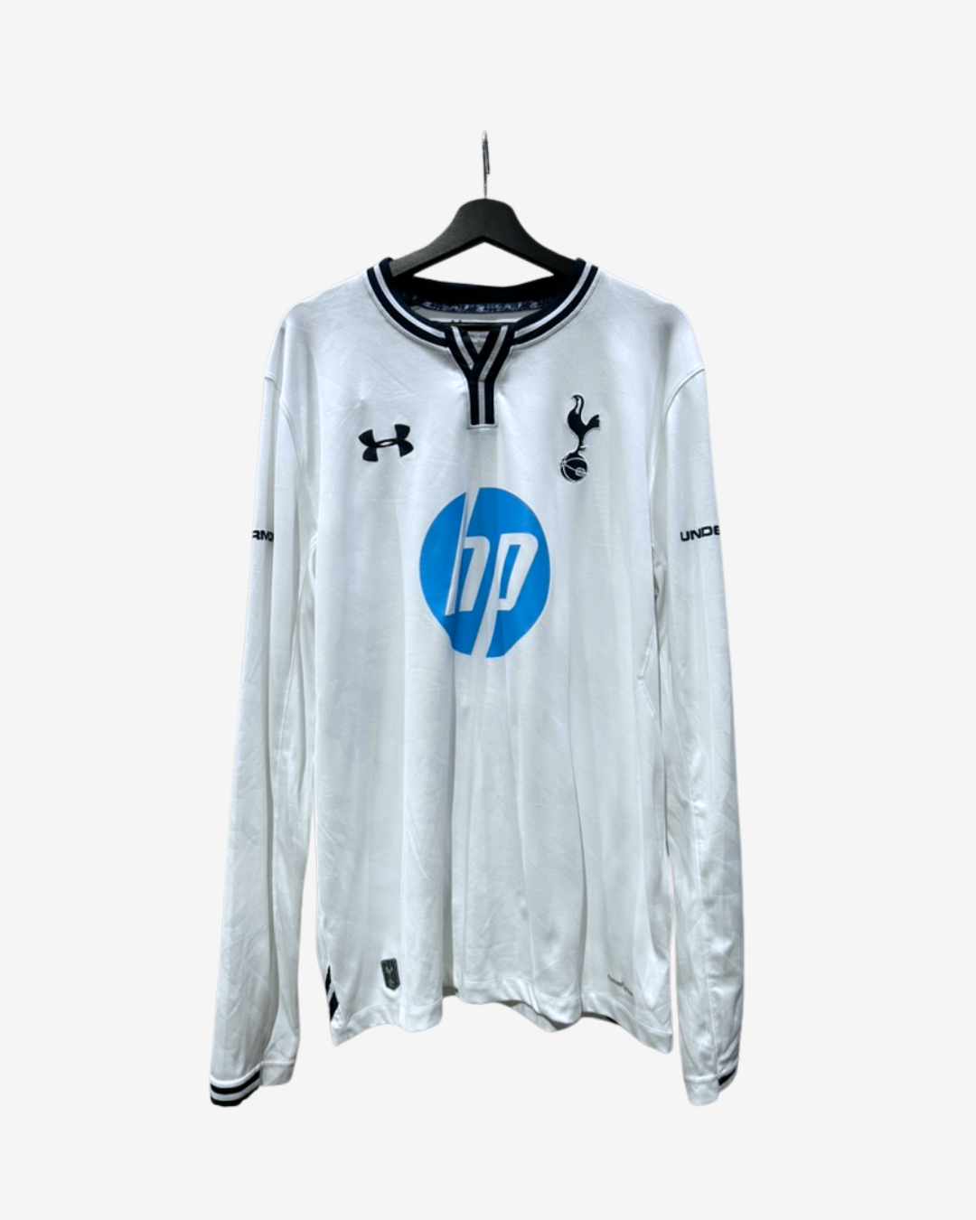 A white long-sleeve Tottenham Hotspur football jersey with black trim and a blue HP logo, hanging on a black hanger against a light gray background.