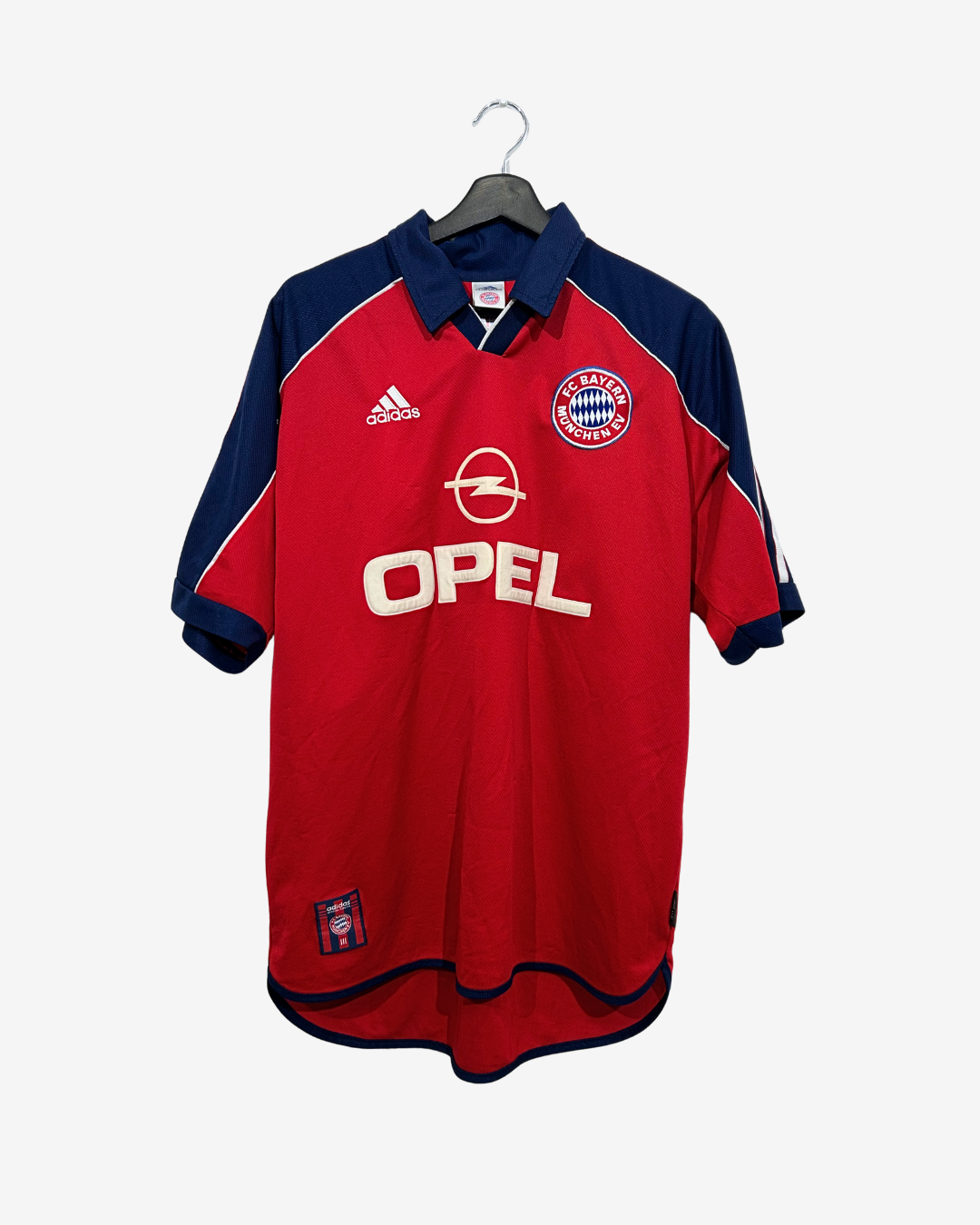 A vintage red and navy blue Adidas Bayern Munich soccer jersey with Opel sponsor logo, hanging on a black hanger against a light gray background.