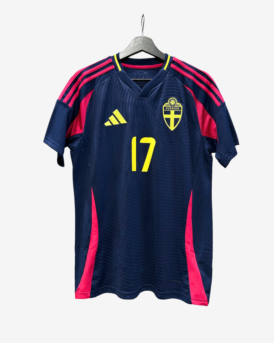 A Sweden national football team Adidas jersey in navy blue with bright pink side panels and shoulder stripes, featuring the yellow number 17 and the Swedish crest on the chest, hanging on a grey hanger against a light grey background.