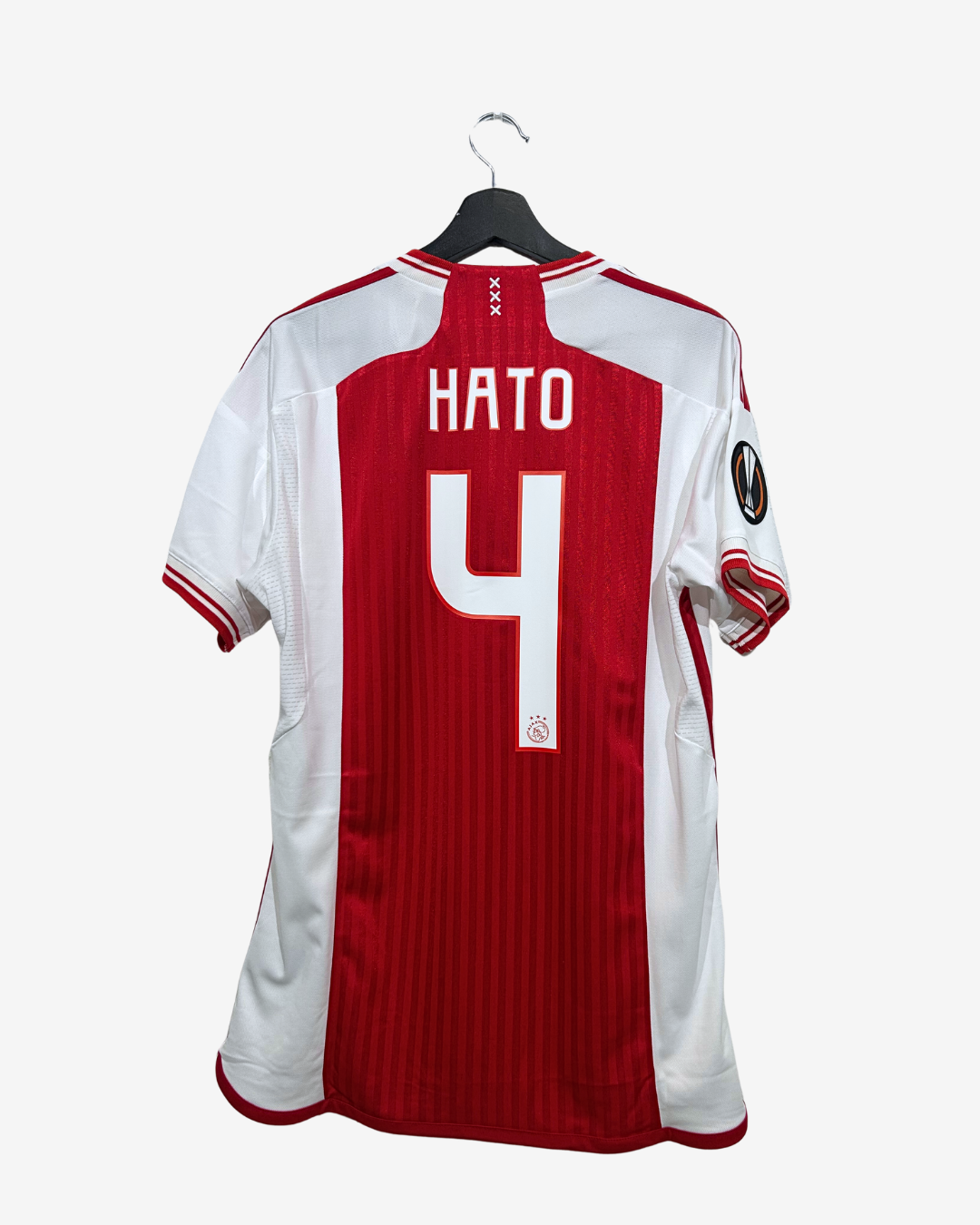 A red and white Netherlands football jersey with 'HATO' and the number '4' on the back, hanging on a black hanger against a light gray background.