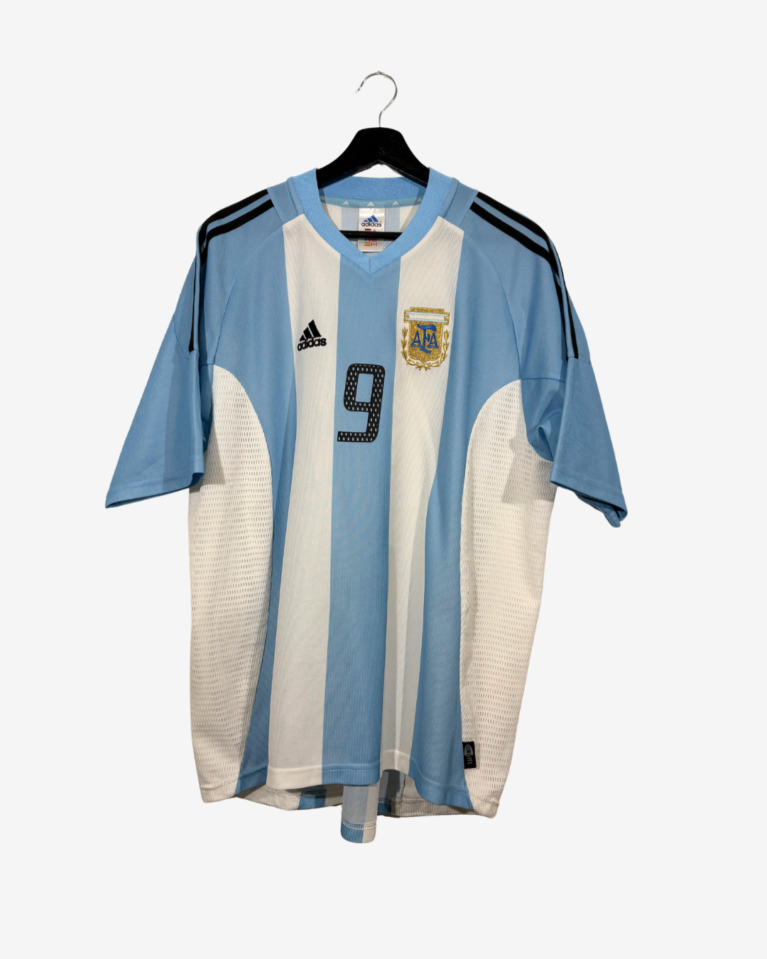 An Argentina national football team home jersey by Adidas, featuring light blue and white vertical stripes with black shoulder stripes and the number 9 on the chest, hanging on a black hanger against a light gray background.