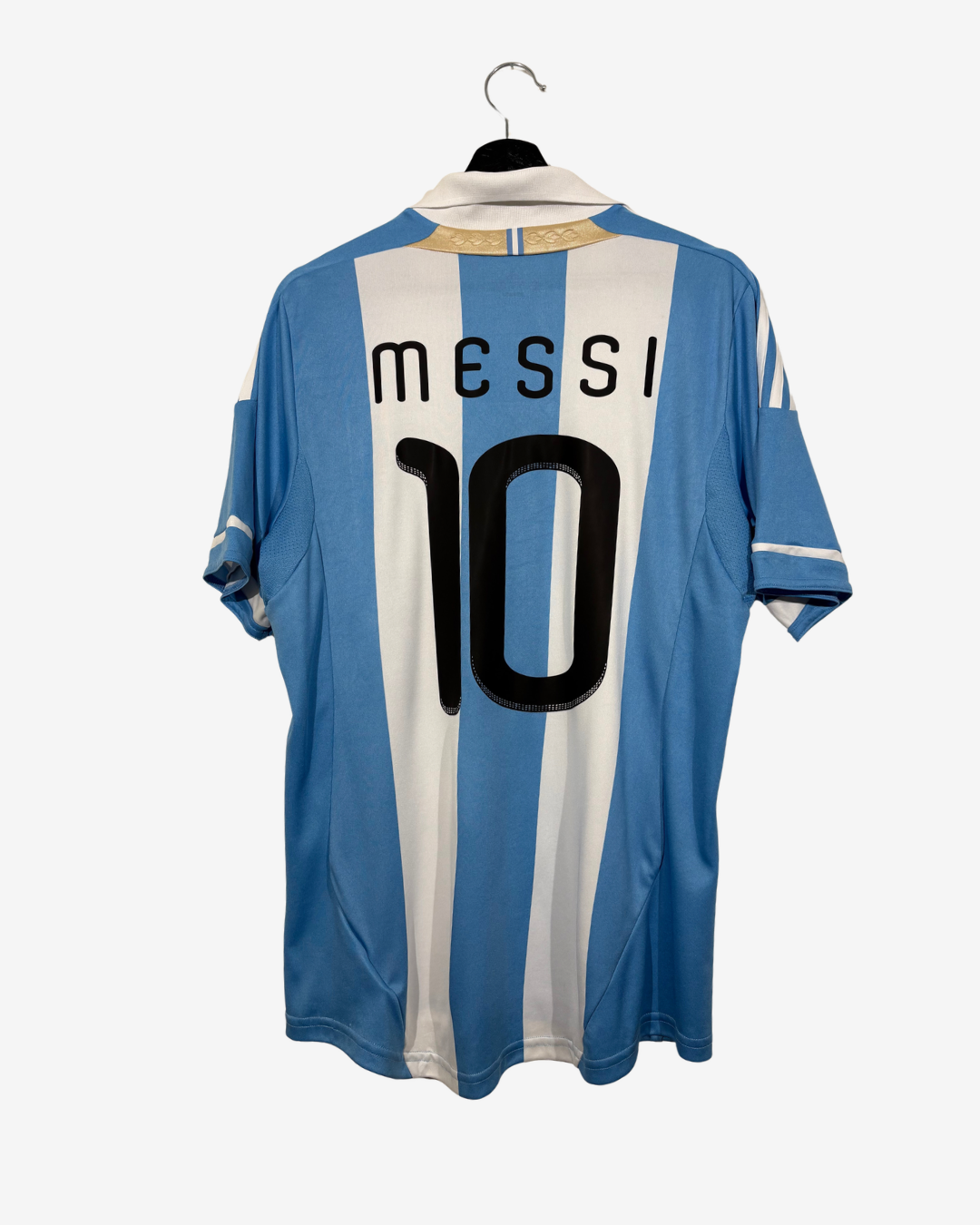 Back view of an Argentina national football team home jersey with light blue and white vertical stripes, featuring 'MESSI' and the number '10' printed in black on the back. The jersey is hanging on a black hanger against a light gray background.