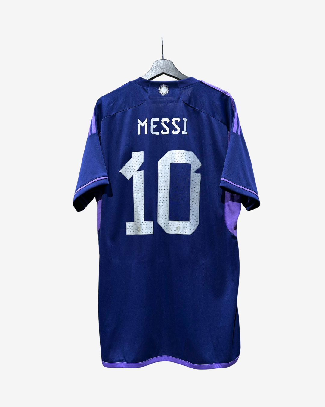 A blue soccer jersey with 'MESSI' and the number '10' printed in white on the back, hanging on a gray hanger against a light gray background.