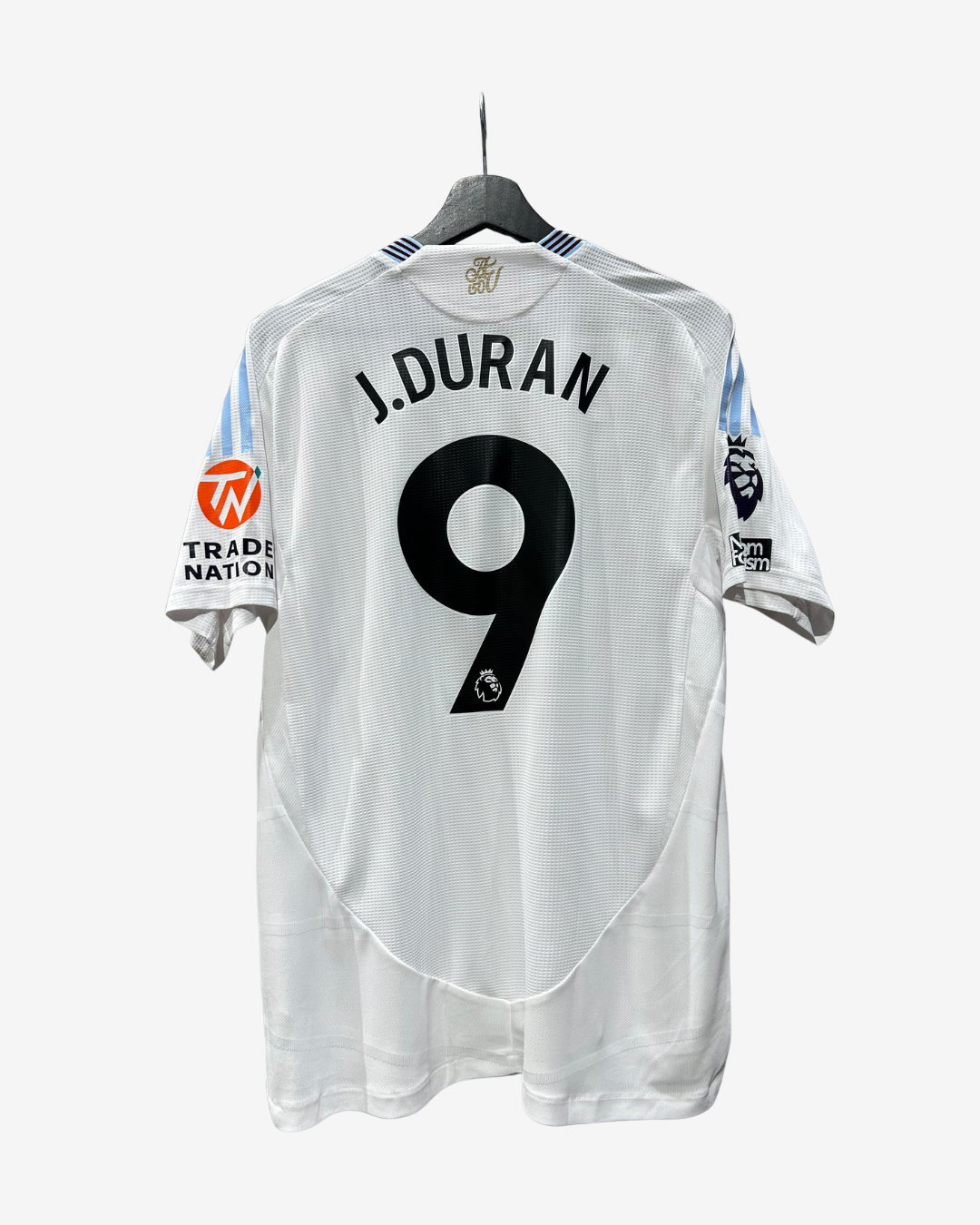 A white Manchester City football jersey with 'J. DURAN' and the number '9' printed on the back, hanging on a black hanger against a light gray background.