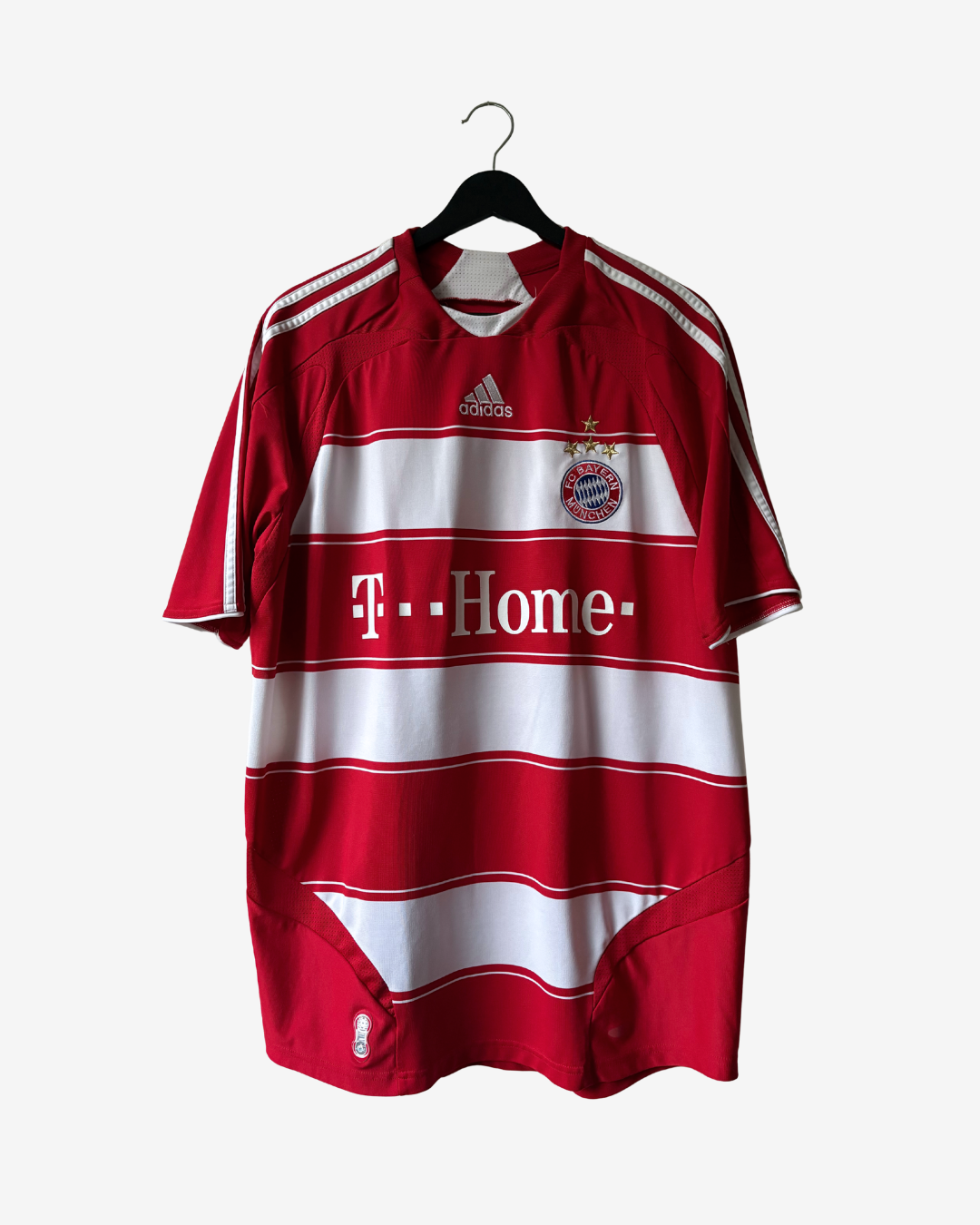 A red and white striped Adidas Bayern Munich soccer jersey hanging on a black hanger against a light gray background. The jersey features the T-Mobile sponsor logo across the chest.