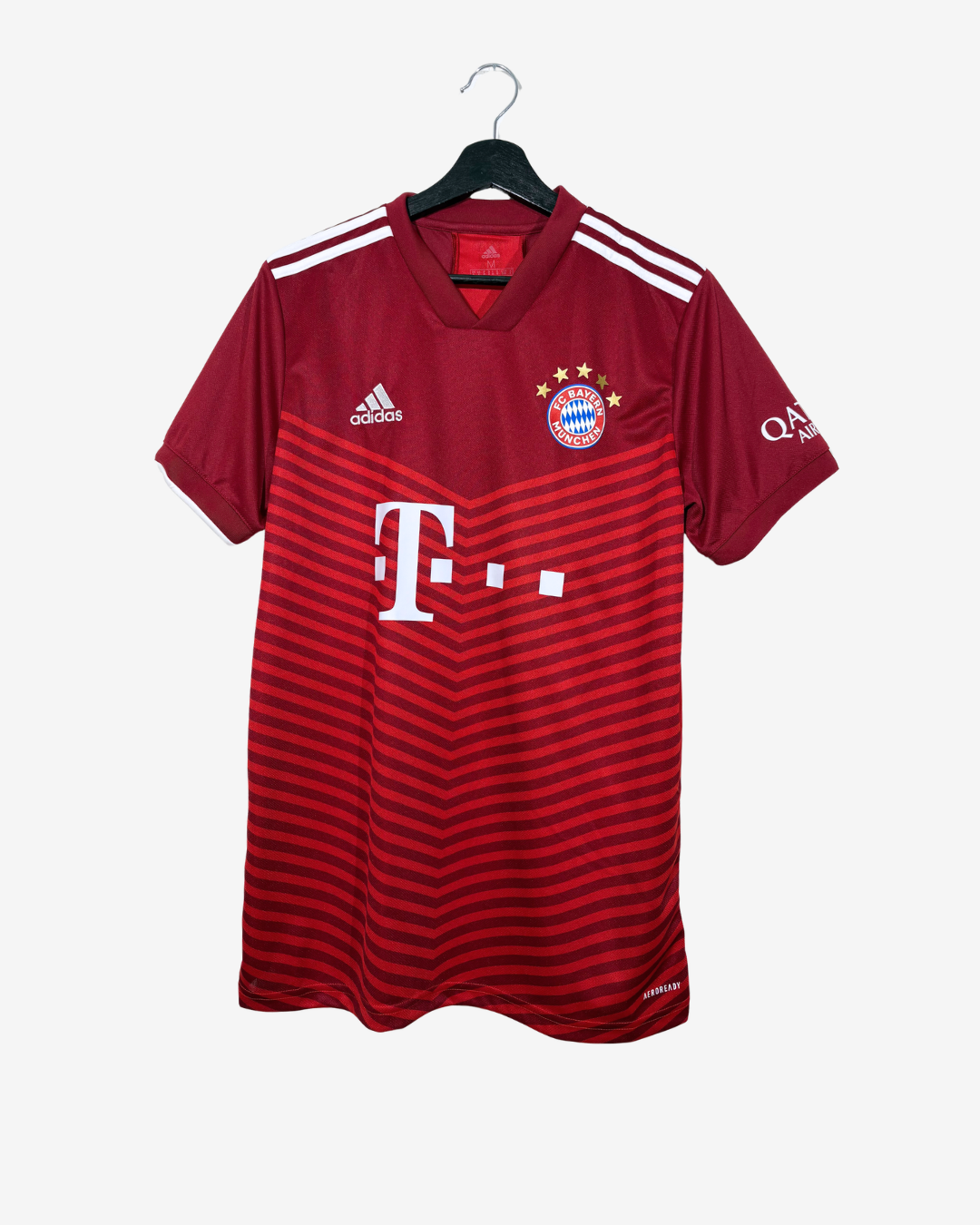 A red and dark red Adidas Bayern Munich soccer jersey hanging on a black hanger against a light gray background. The jersey features the white Adidas logo on the right chest, the Bayern Munich club crest on the left chest, and the large white T-Mobile sponsor logo across the center.
