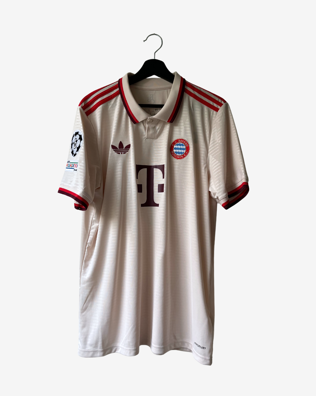 A vintage Adidas Bayern Munich home soccer jersey in cream with red and navy accents, hanging on a black hanger against a light gray background.