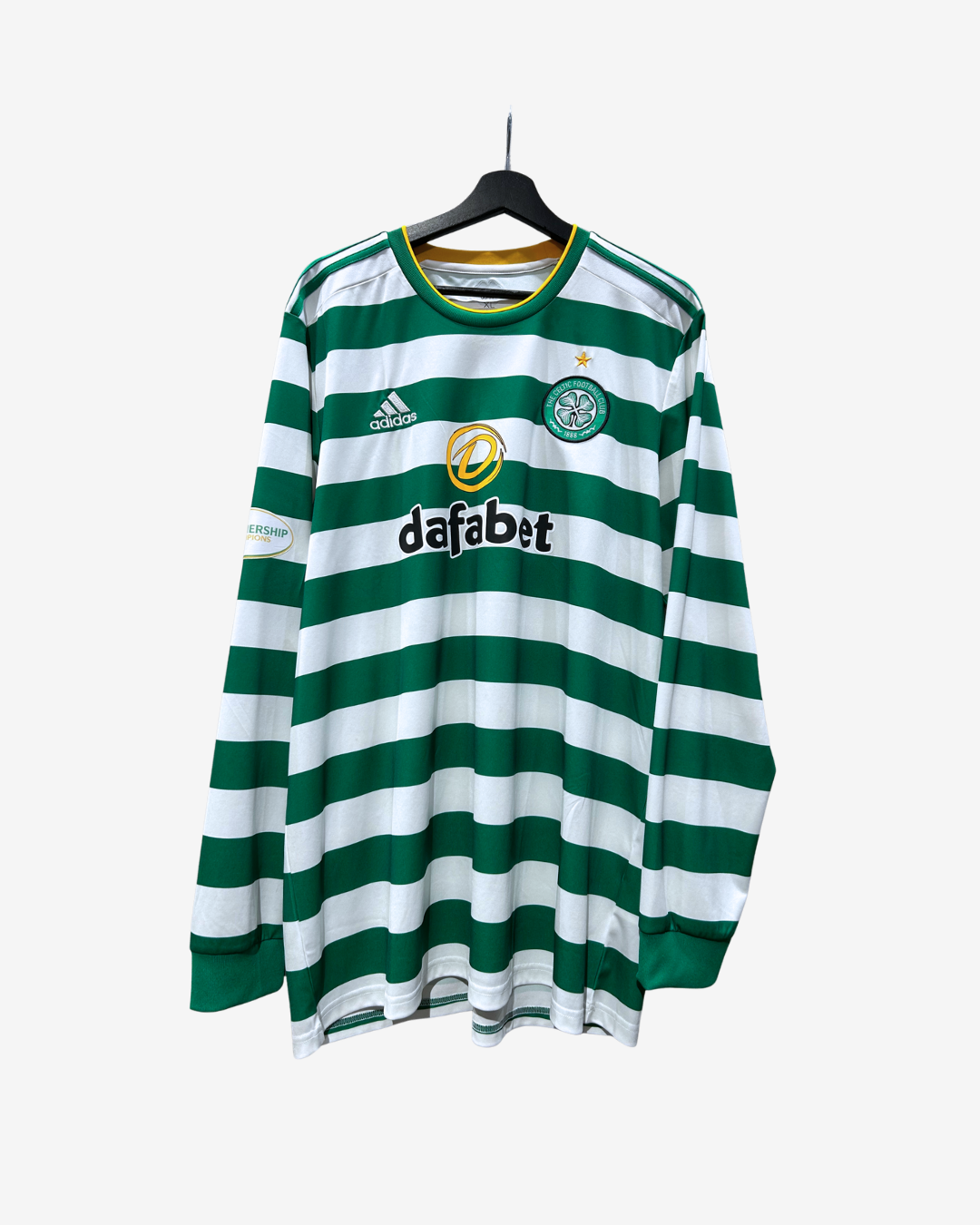 A long-sleeve Celtic FC soccer jersey with green and white horizontal stripes, featuring the Adidas logo on the right chest, the Celtic crest on the left chest, and the 'dafabet' sponsor logo in the center. The jersey is shown hanging on a black hanger against a light gray background.