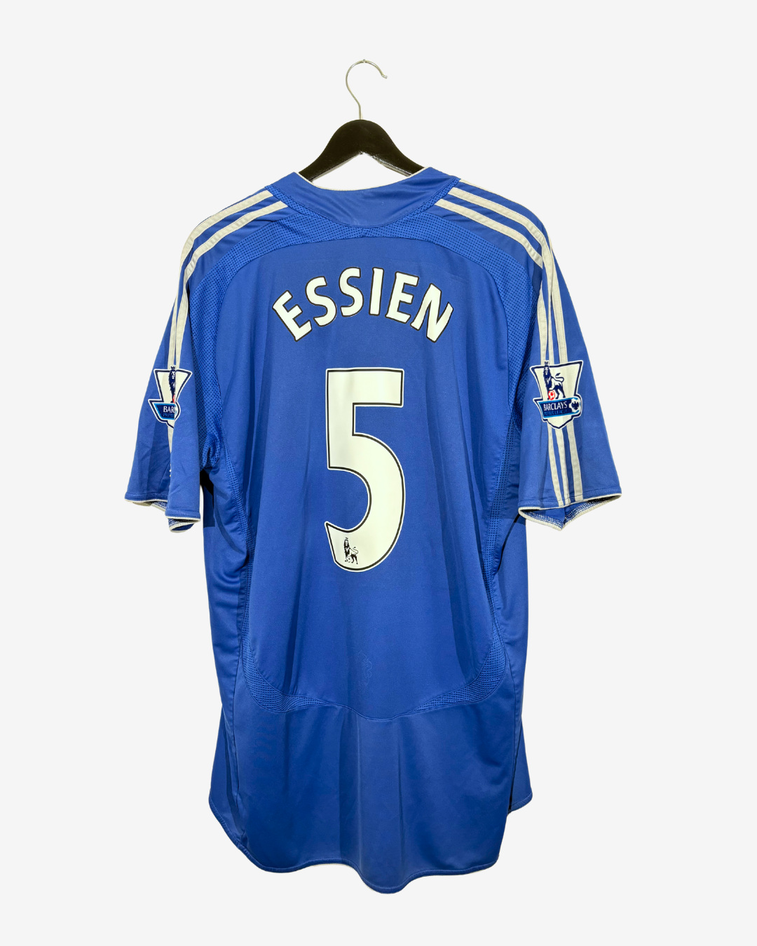 A blue Chelsea football jersey with 'ESSIEN' and the number '5' on the back, hanging on a black hanger against a light gray background.