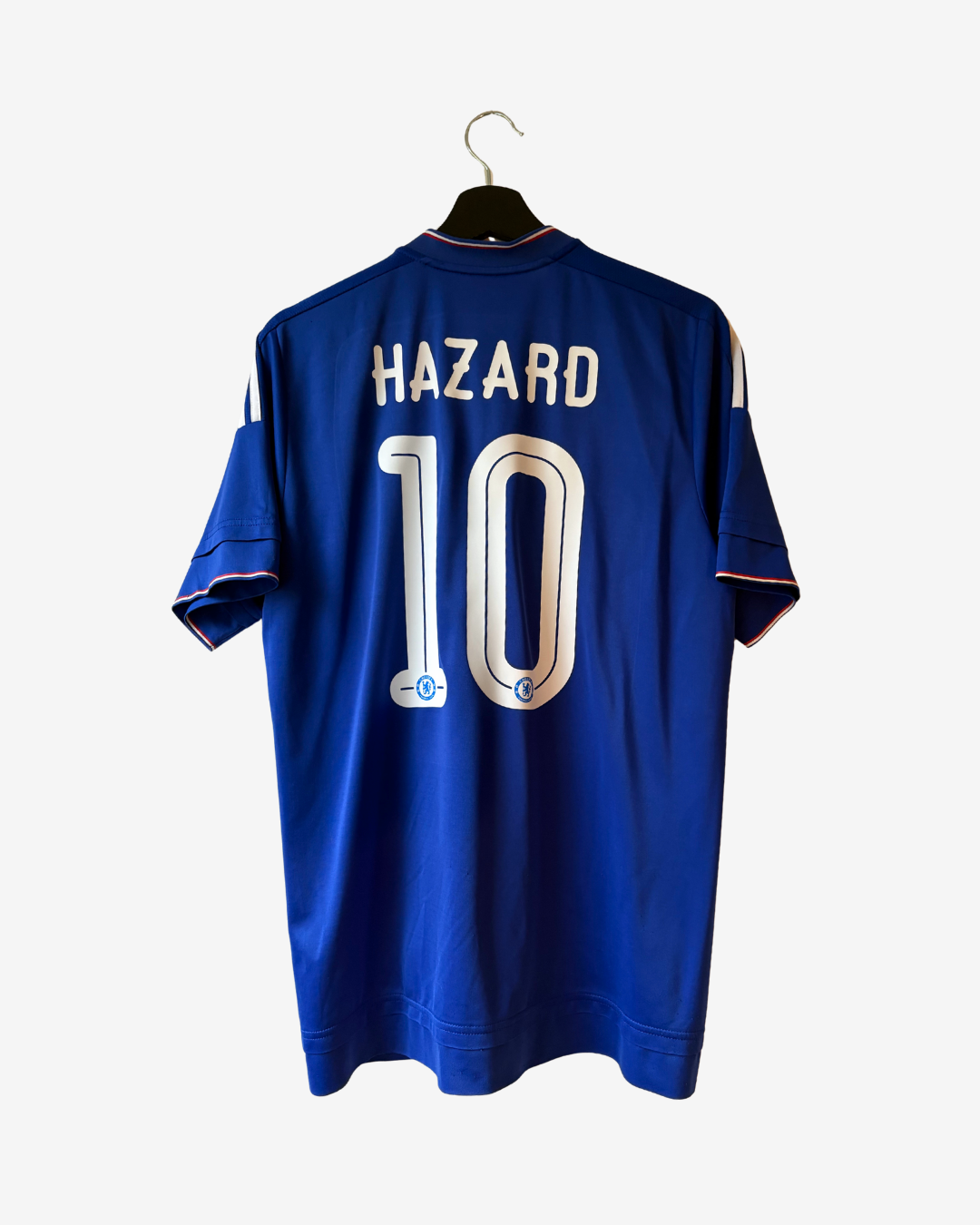 A royal blue Chelsea football jersey with 'HAZARD' and the number '10' printed on the back, hanging on a black hanger against a light gray background.