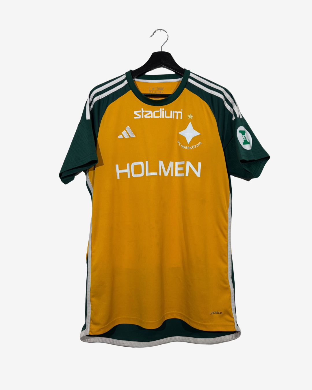 A yellow and dark green Adidas IFK Norrköping soccer jersey hanging on a black hanger against a light gray background. The jersey features white stripes on the shoulders, a white 'stadium' sponsor logo, the Adidas logo