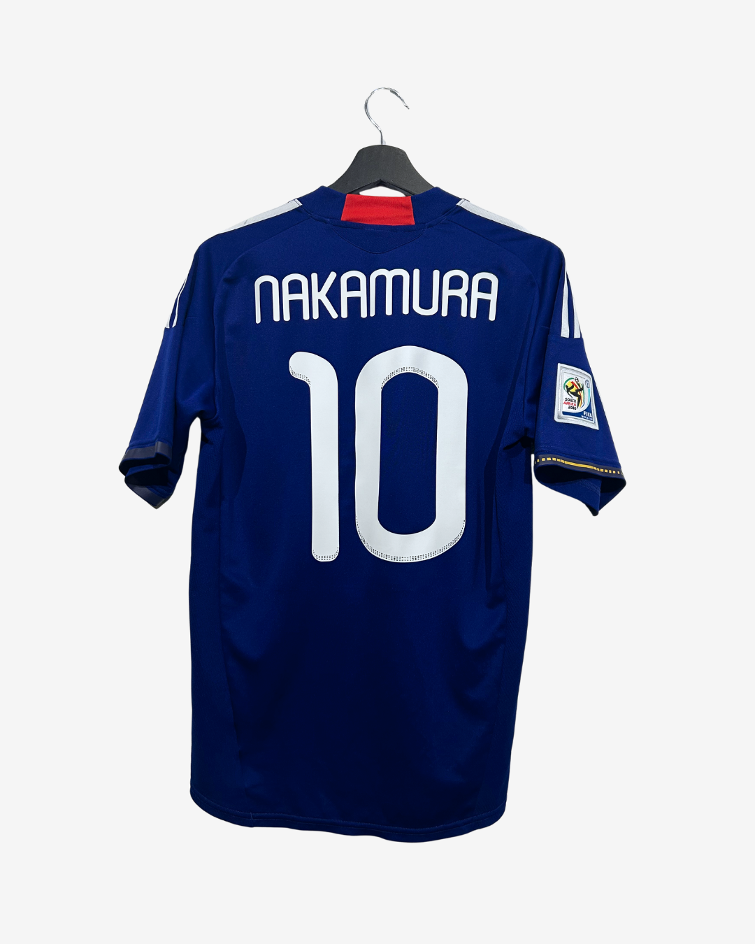 A dark blue soccer jersey with 'NAKAMURA' and the number '10' in white on the back, hanging on a black hanger against a light gray background.