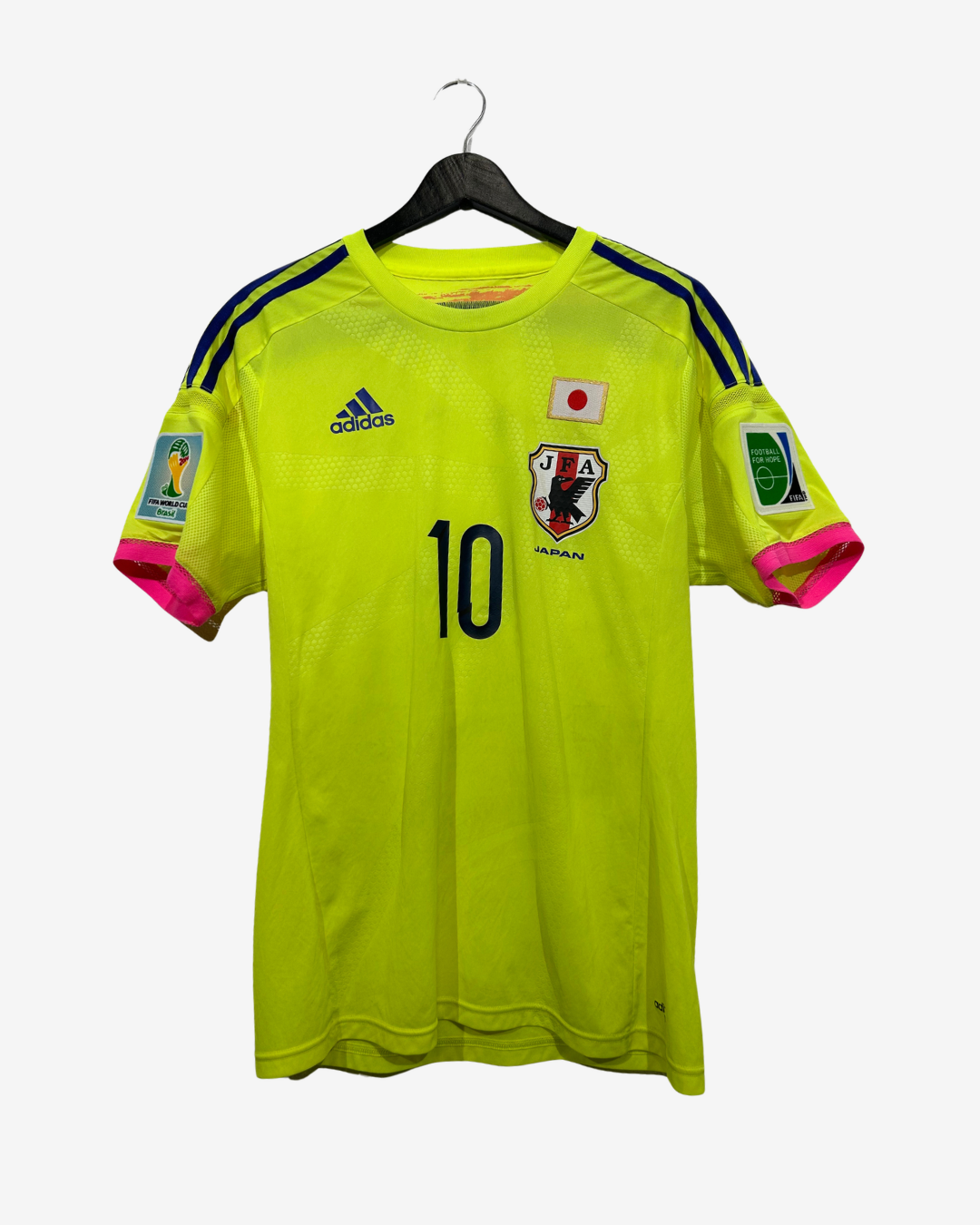 A bright neon yellow Japan national team soccer jersey with number 10, hanging on a black hanger against a light gray background. The jersey features navy blue shoulder stripes, a white Adidas logo, a Japanese flag patch, a JFA crest, and World Cup 2022 patches on the sleeves.