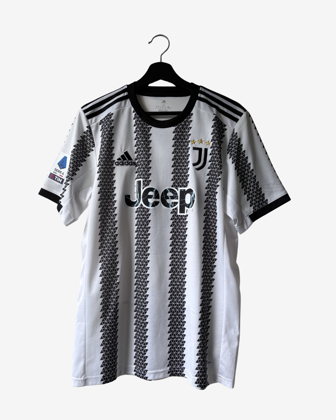 A white and black striped Juventus soccer jersey by Adidas, featuring the Jeep logo on the front, hanging on a black hanger against a light gray background.