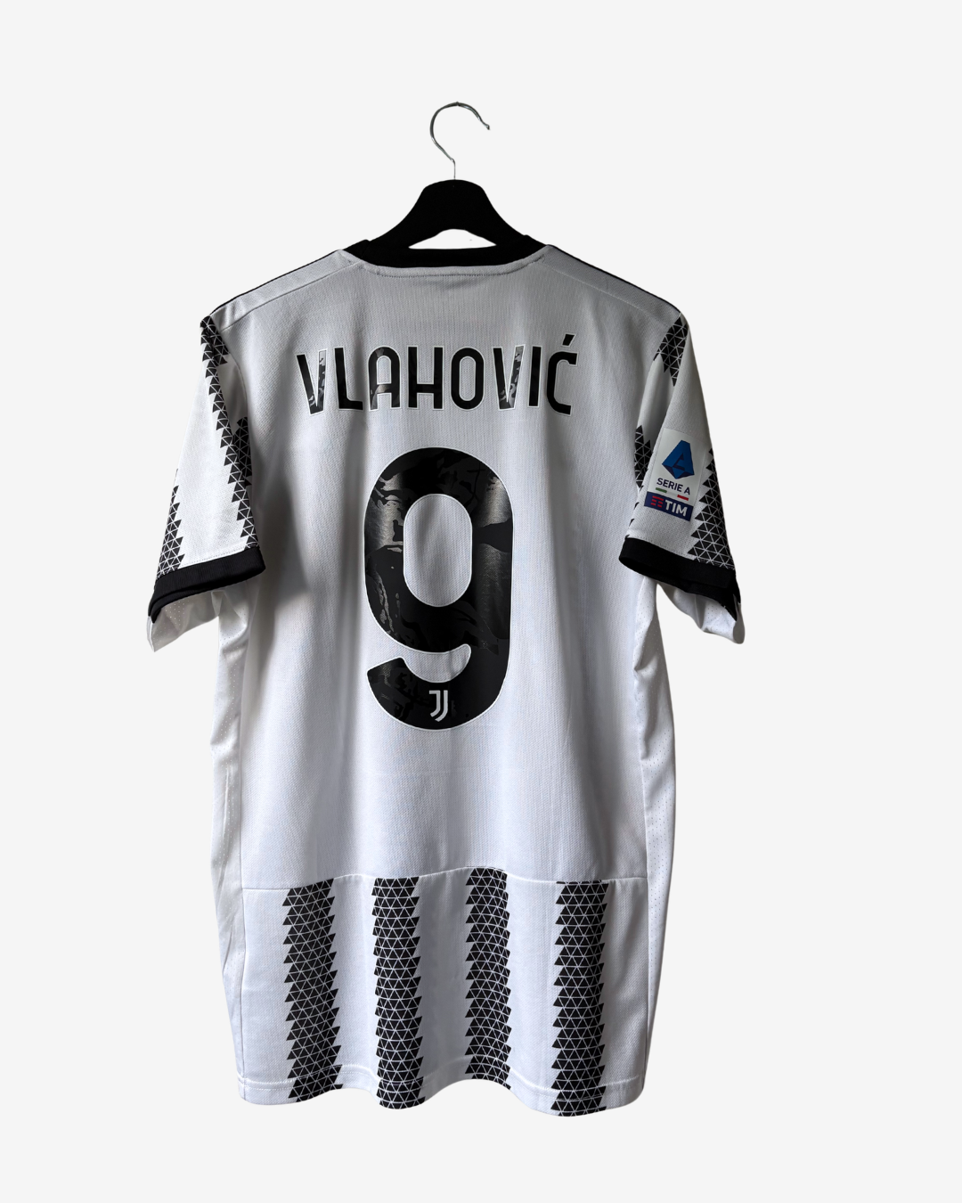 White and black Juventus home jersey with 'VLAHOVIČ' and number 9 printed on the back, hanging on a black hanger against a light gray background.