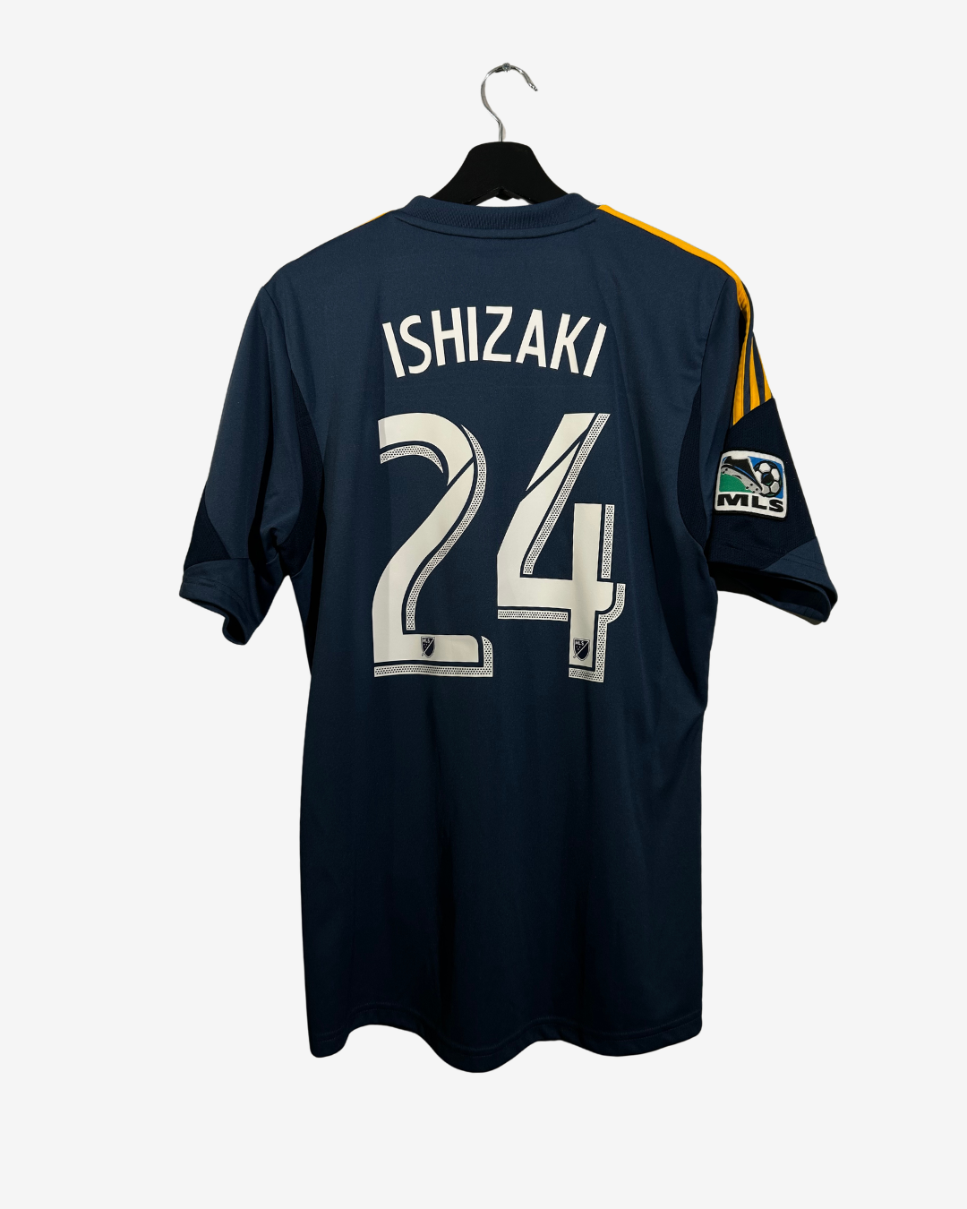 Back view of a dark navy blue soccer jersey hanging on a black hanger against a light gray background. The jersey features the name 'ISHIZAKI' and number '24' in white with a black outline on the back, and yellow stripes on the sleeve.