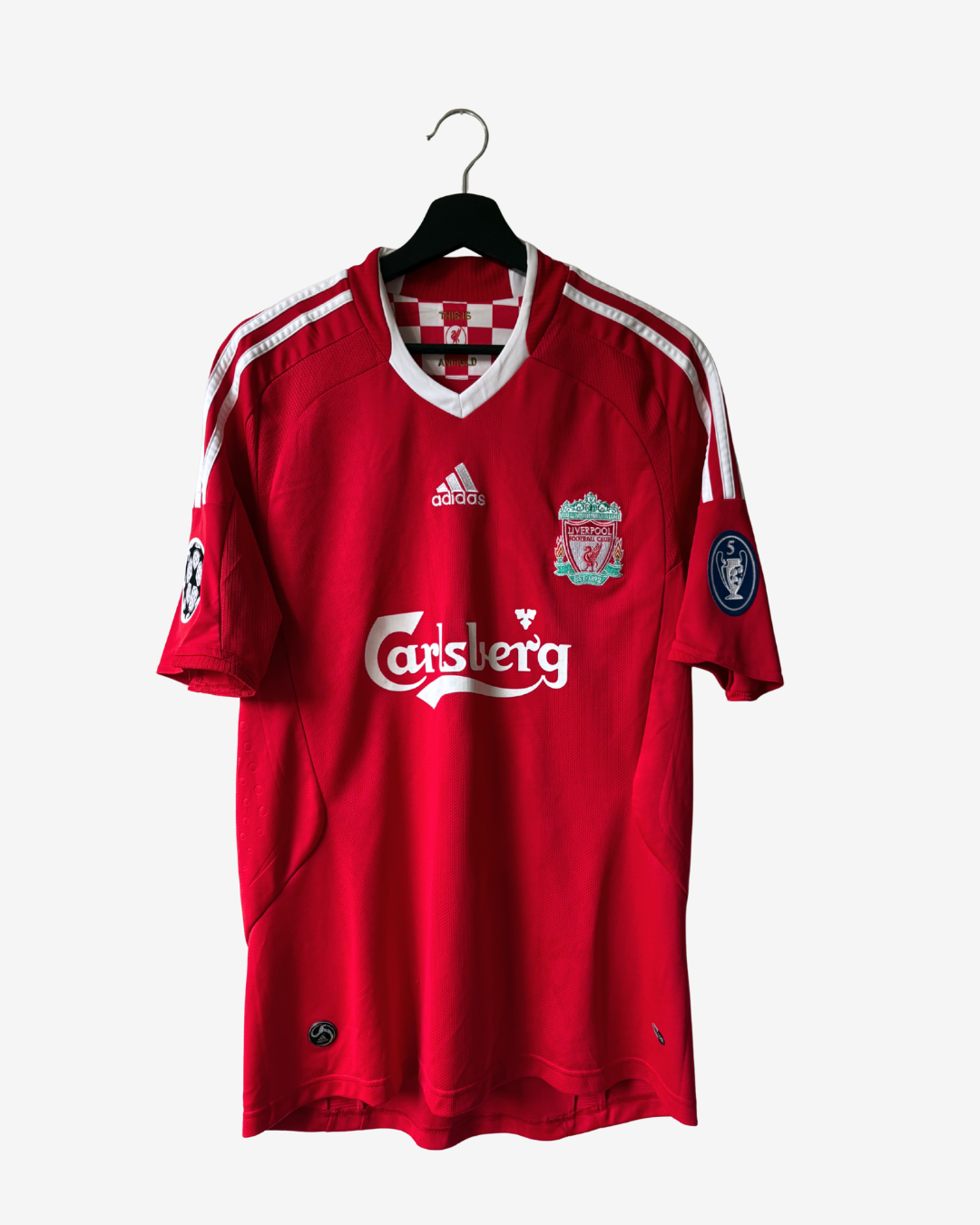 A red Adidas Liverpool football jersey with Carlsberg sponsor logo, hanging on a black hanger against a light gray background.