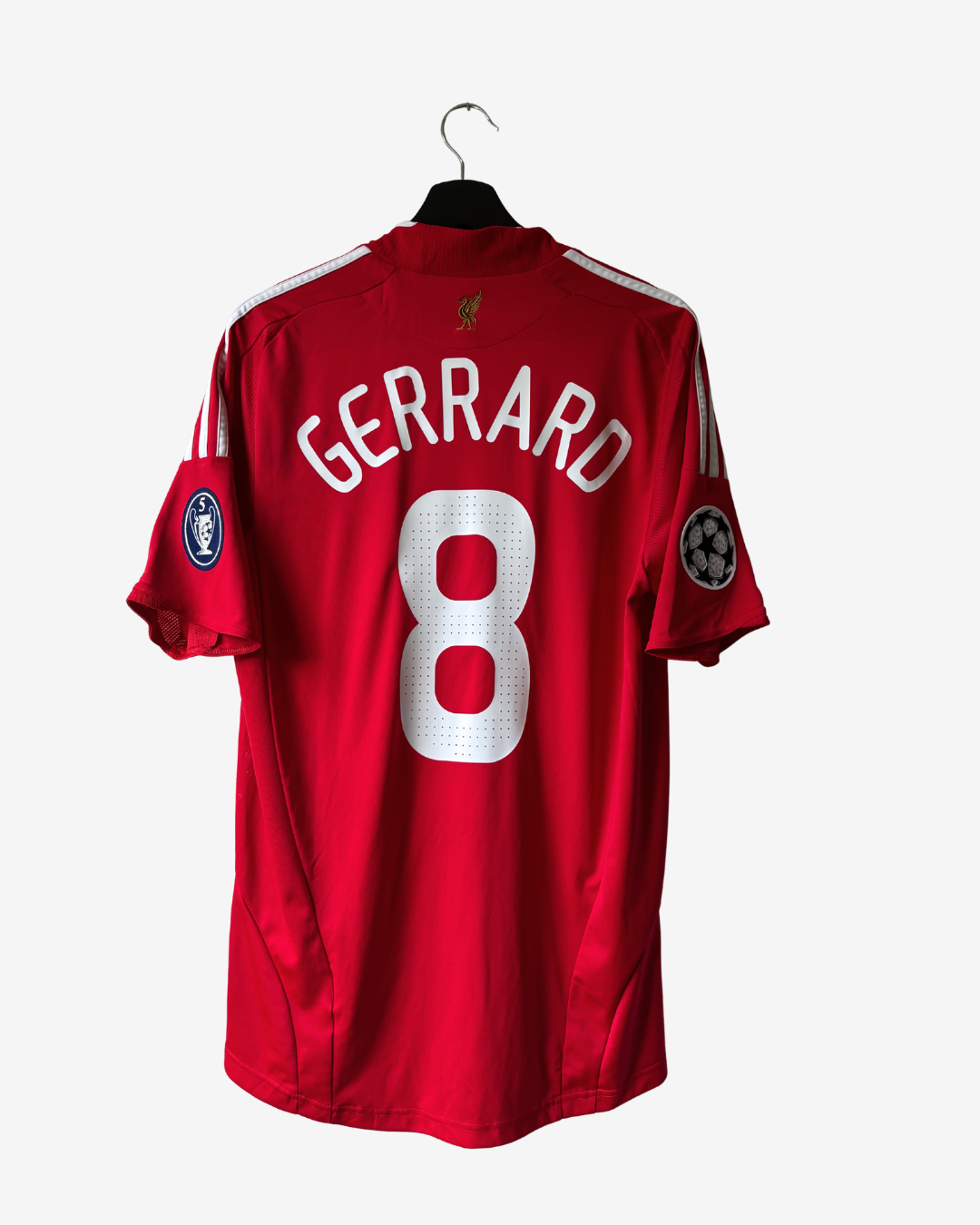 A red Liverpool football jersey with 'GERRARD' and the number '8' on the back, hanging on a black hanger against a light gray background.