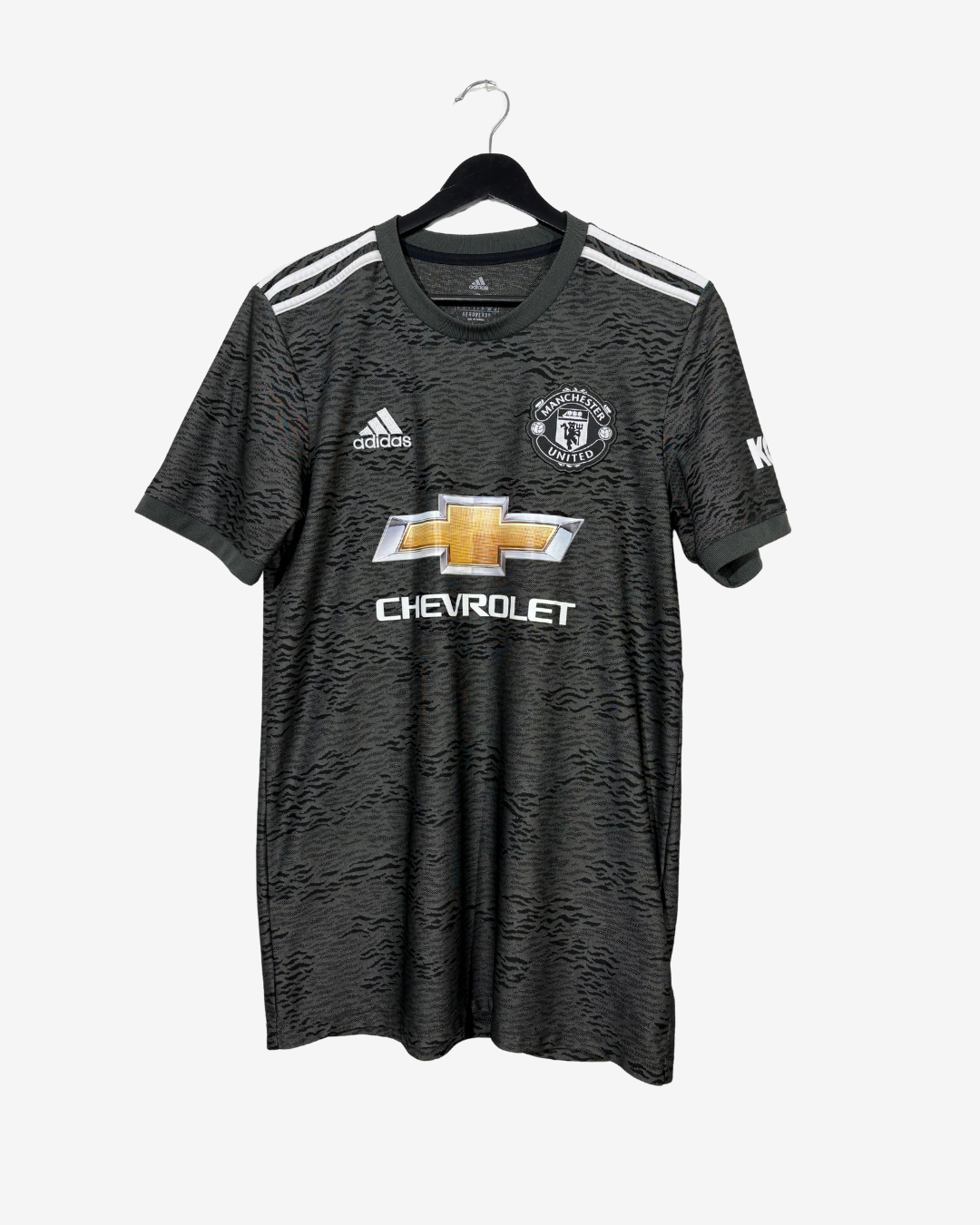 A black Manchester United soccer jersey with a subtle textured pattern, featuring white shoulder stripes, the Adidas logo, the Manchester United crest, and the Chevrolet sponsor logo. The jersey is displayed on a black hanger against a light gray background.