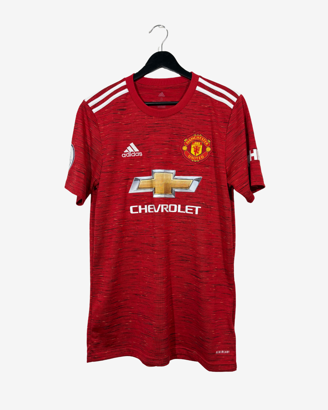 A red Manchester United home soccer jersey by Adidas, featuring the gold Chevrolet logo and club crest, hanging on a black hanger against a light gray background.