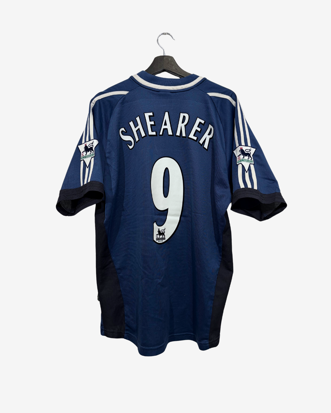 A blue and white football jersey hanging on a black hanger against a light gray background. The back of the shirt features the name 'SHEARER' in white arched lettering above a large white number '9'.