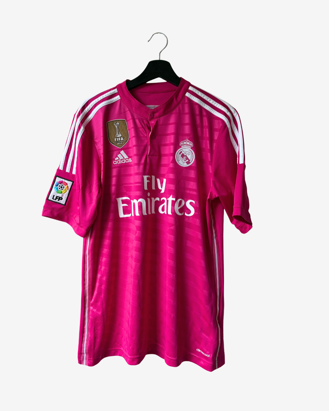 A pink Real Madrid soccer jersey with white stripes and logos, hanging on a black hanger against a light gray background.