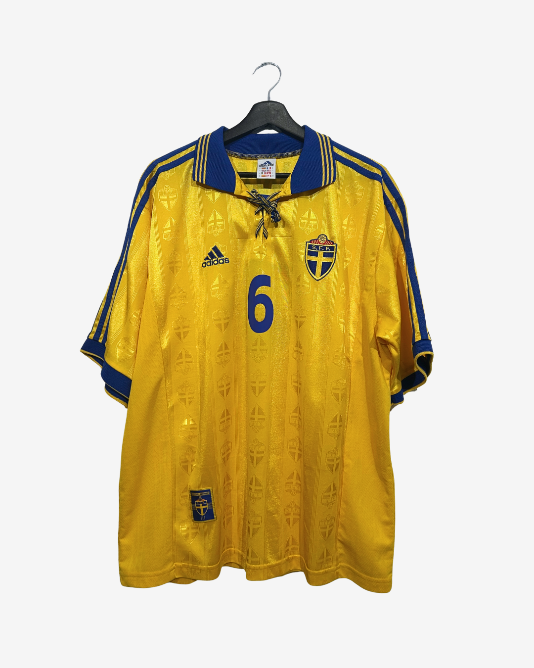 A vintage yellow Sweden national football team jersey with blue trim, featuring the Adidas logo, the number 6 on the front, and the Swedish crest, hanging on a black hanger against a light gray background.