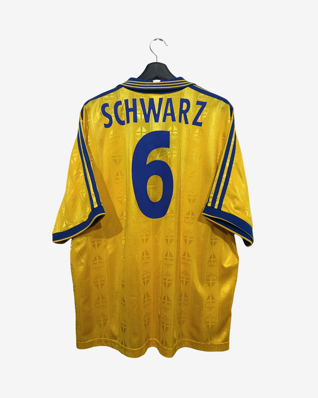 A yellow soccer jersey with 'SCHWARZ' and the number '6' printed in blue on the back, hanging on a black hanger against a light gray background.