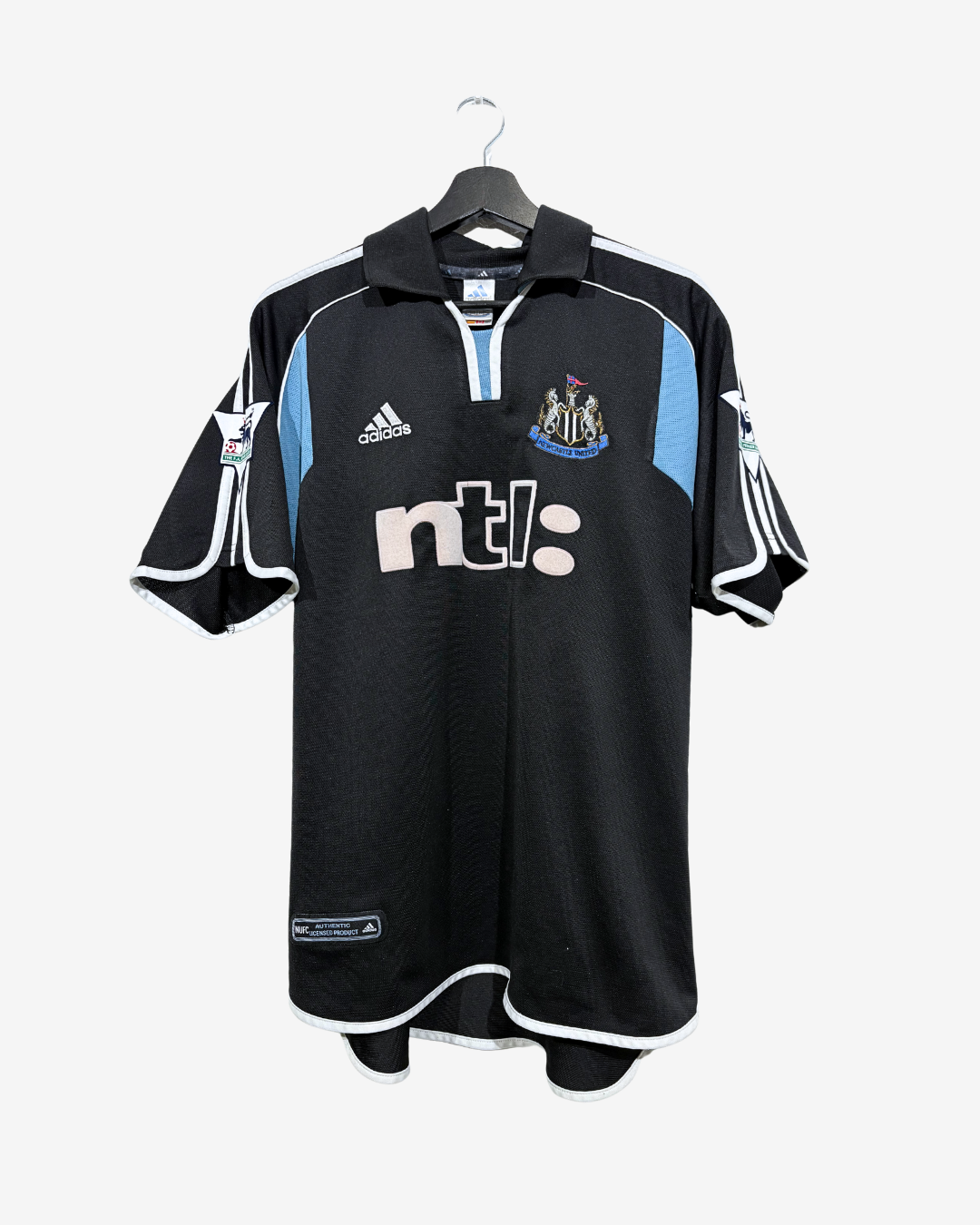 A black Adidas Newcastle United football shirt with light blue and white accents, hanging on a black hanger against a light gray background.