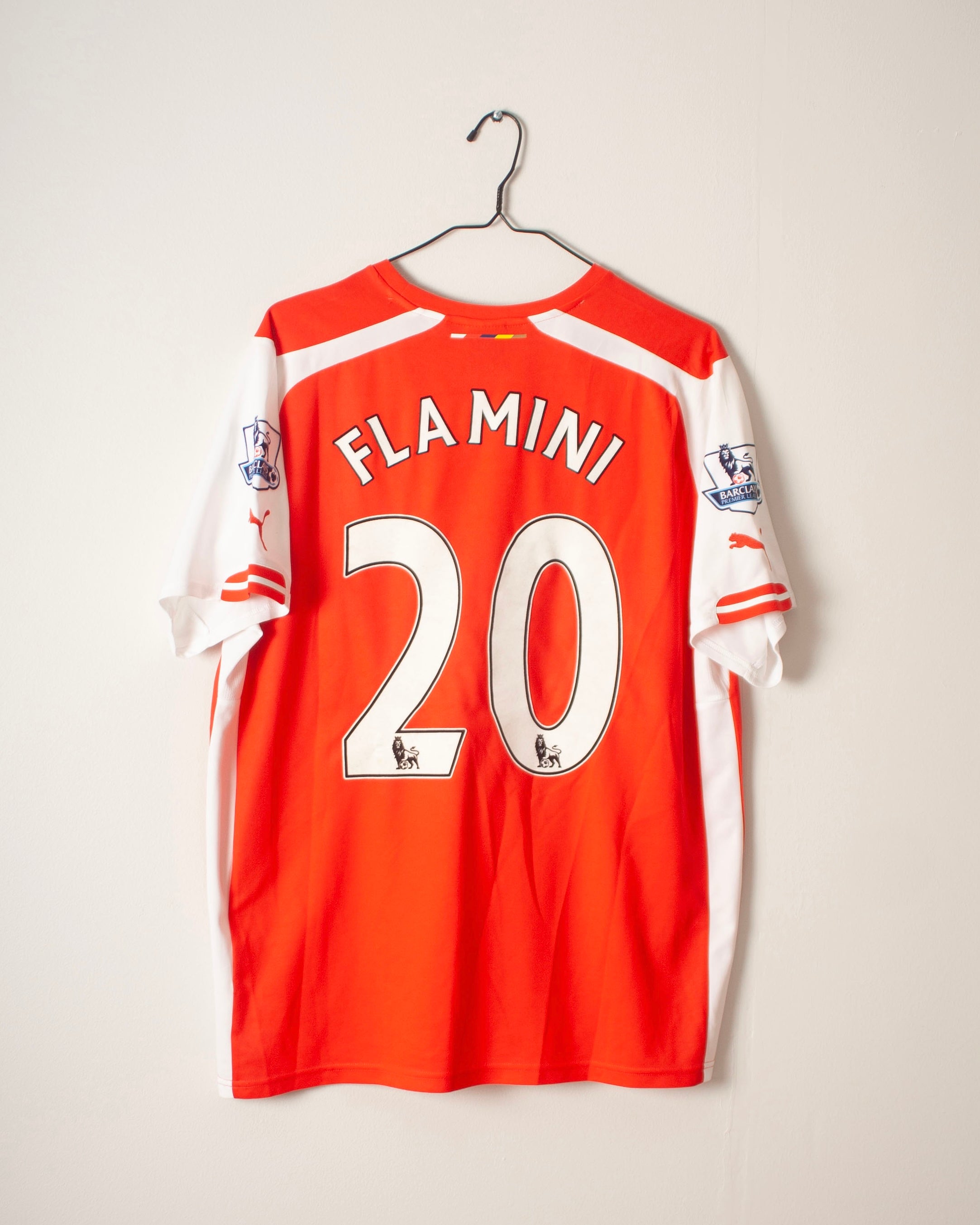 Red sports jersey with 'Flamini 20' on a hanger against a white background