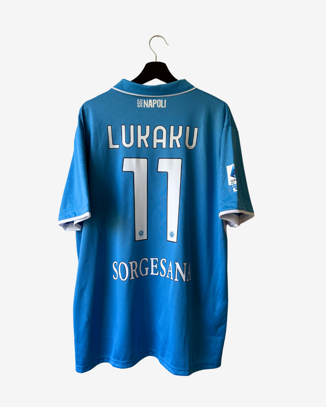 A blue soccer jersey hanging on a black hanger against a light gray background. The back of the jersey features the name 'LUAKU' and number '11' in white, with 'NAPOLI' printed at the collar and 'SORGESANA' near the hem.