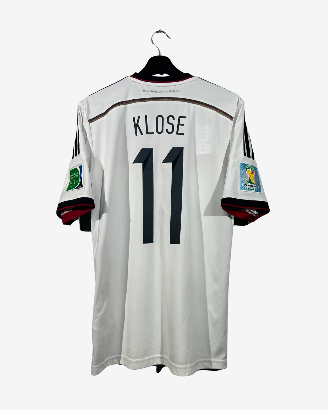 A white Germany national team soccer jersey with 'KLOSE' and the number '11' on the back, hanging on a black hanger against a light gray background.
