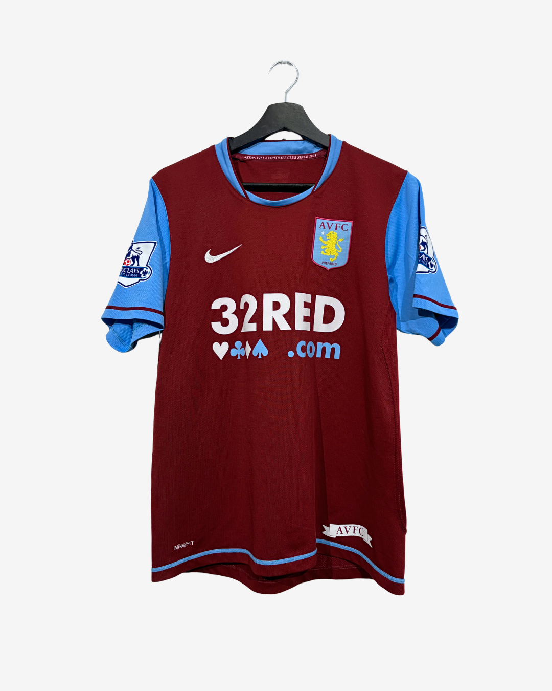 A vintage Aston Villa football jersey in maroon and light blue, hanging on a black hanger against a light gray background. The jersey features the club's crest, a Nike swoosh, and a 32RED.