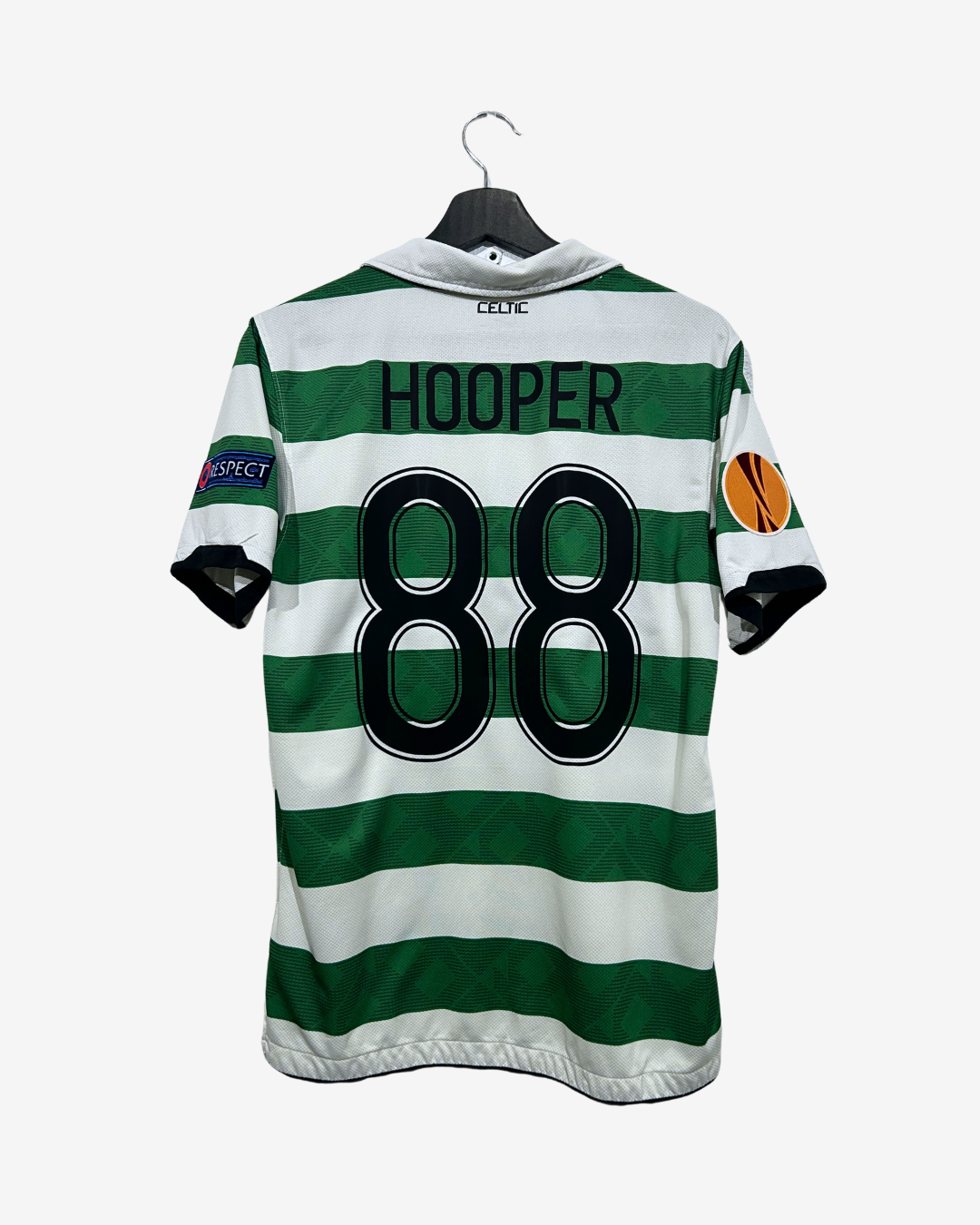 Back view of a Celtic FC football jersey with green and white horizontal stripes, featuring the name 'HOOPER' and number '88' in black on the back, hanging on a black hanger against a light gray background.