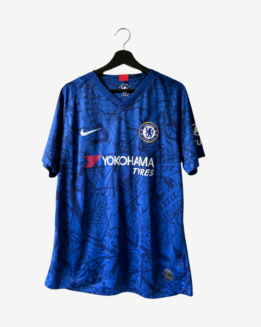 A blue Chelsea FC soccer jersey with a subtle tonal pattern, featuring the white Nike swoosh and Yokohama Tires logos, hanging on a black hanger against a light gray background.