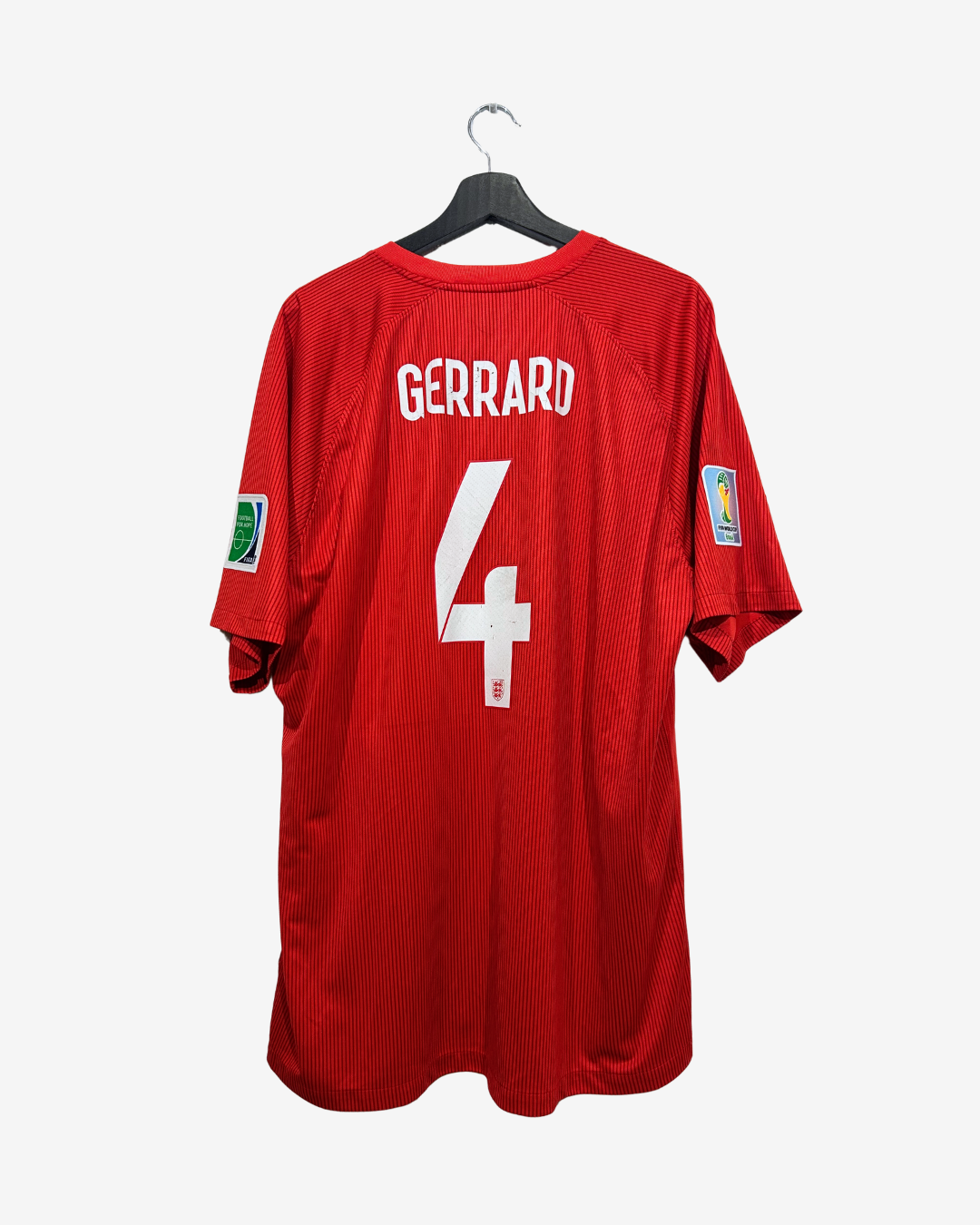 A red short-sleeve soccer jersey hanging on a black hanger against a light gray background. The back of the shirt features the name 'GERRARD' in white block letters above a large white number '4'.