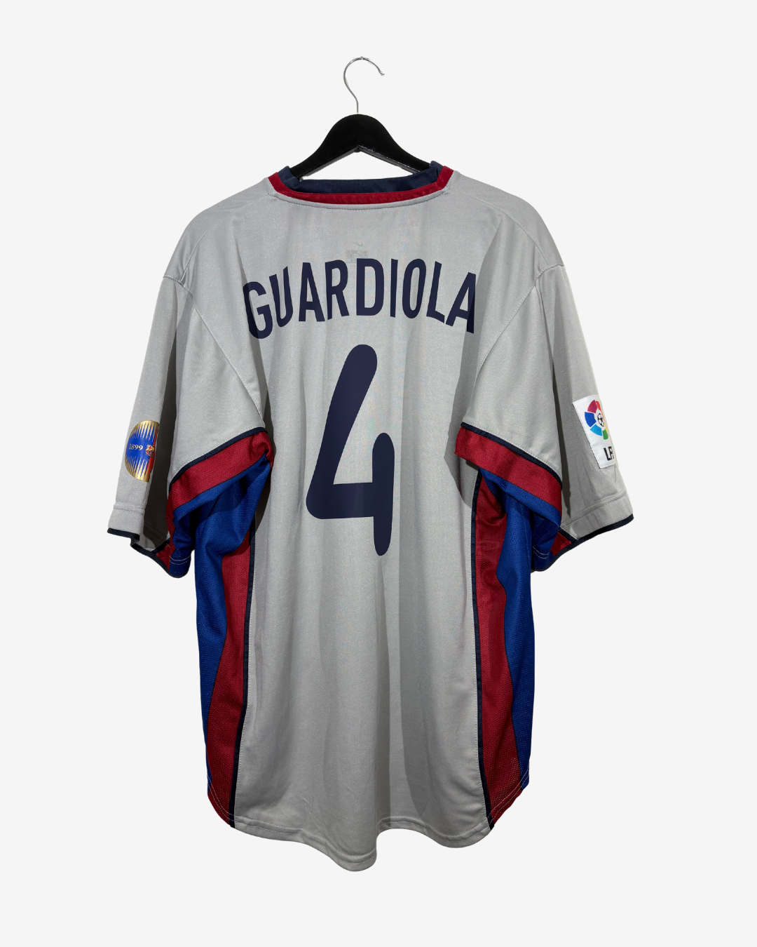 A vintage FC Barcelona home jersey with 'GUARDIOLA 4' printed on the back, hanging on a black hanger against a light gray background.
