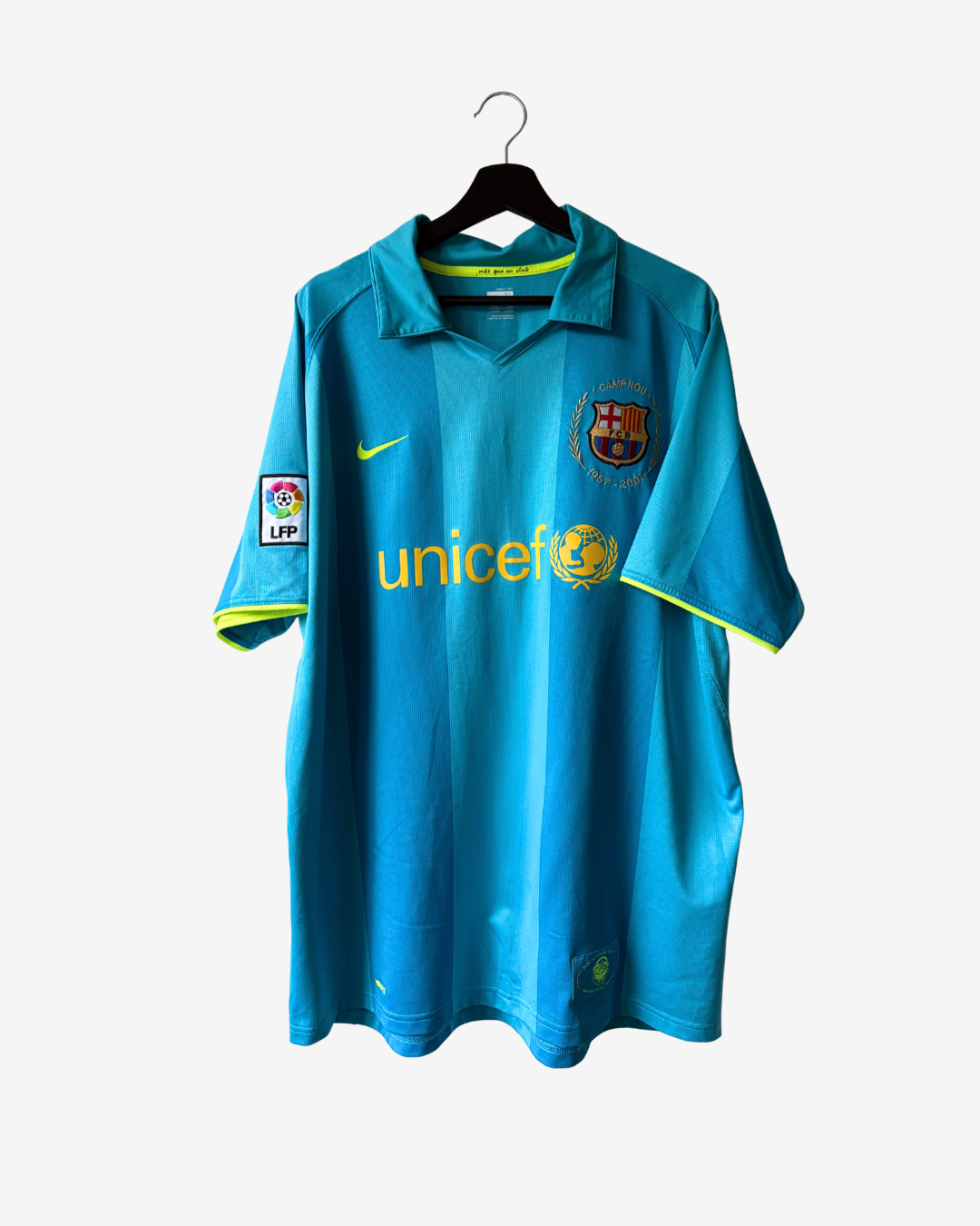 A light blue FC Barcelona soccer jersey with yellow accents, featuring the 'unice' sponsor logo across the chest, a Nike swoosh, and the LFP patch on the sleeve, hanging on a black hanger against a light gray background.