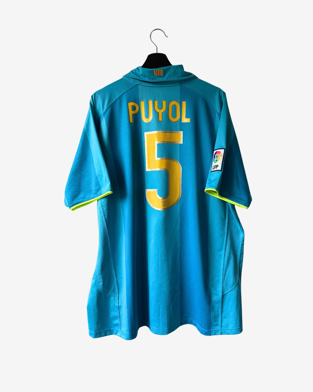 A blue soccer jersey with 'PUYOL' and the number '5' in yellow on the back, hanging on a black hanger against a light gray background.