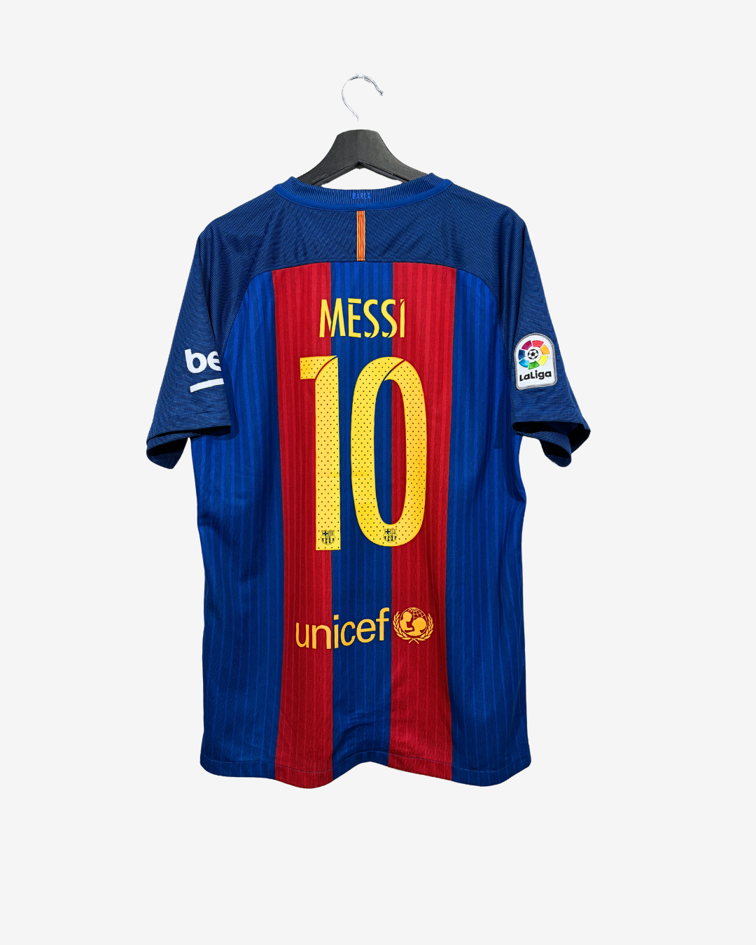 The back of a blue and red striped FC Barcelona soccer jersey with 'MESSI 10' printed in yellow, hanging on a black hanger against a light gray background.