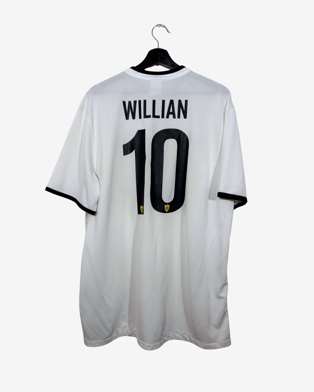 White short-sleeve soccer jersey shown from the back on a black hanger against a light gray background. The back features the name 'WILLIAN' and the number '10' in black, with small yellow accents below the number.